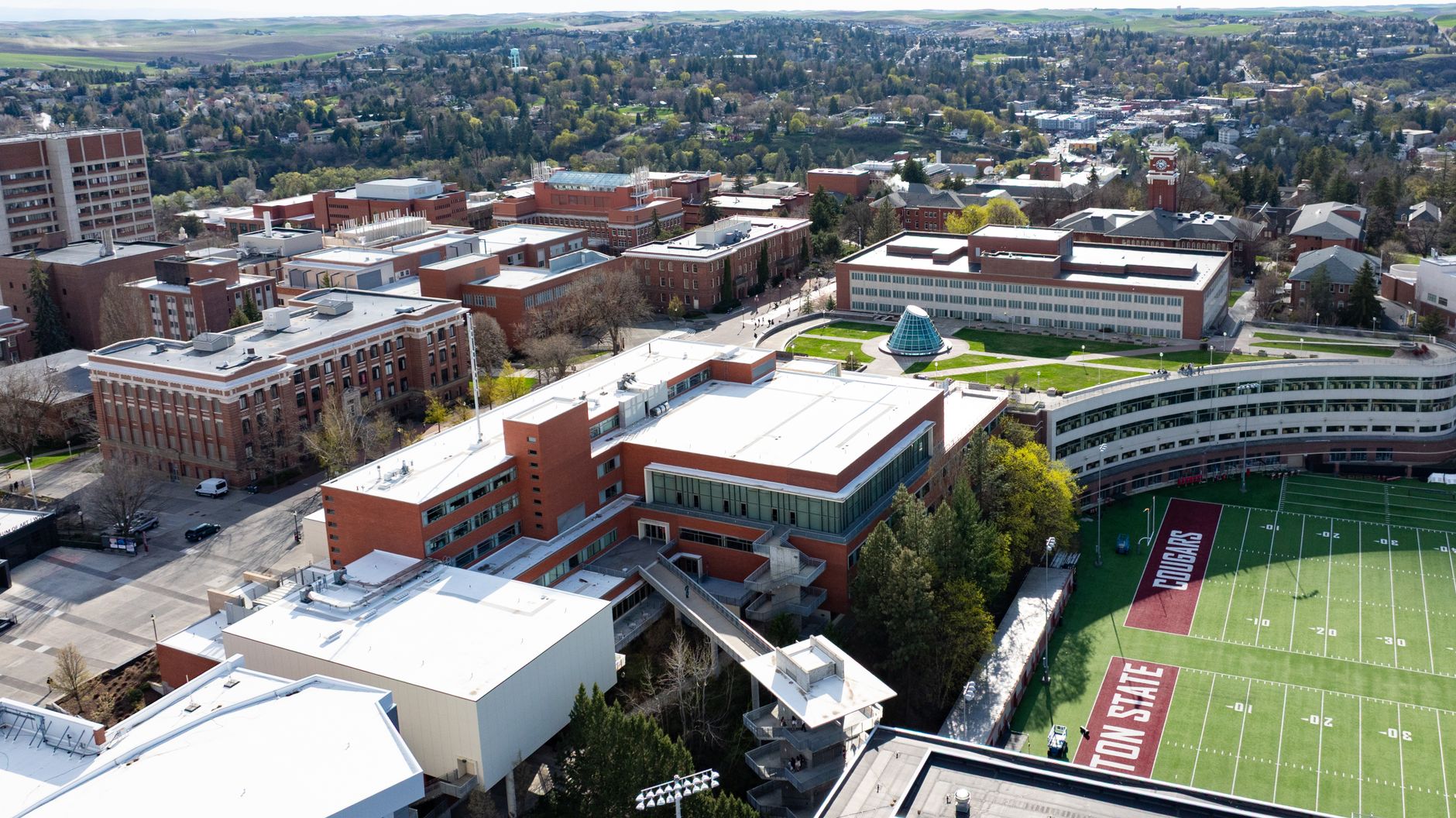 An aerial shot looking down on a large university football stadium, showing the complex roof structure that is challenging and time-consuming to inspect manually.