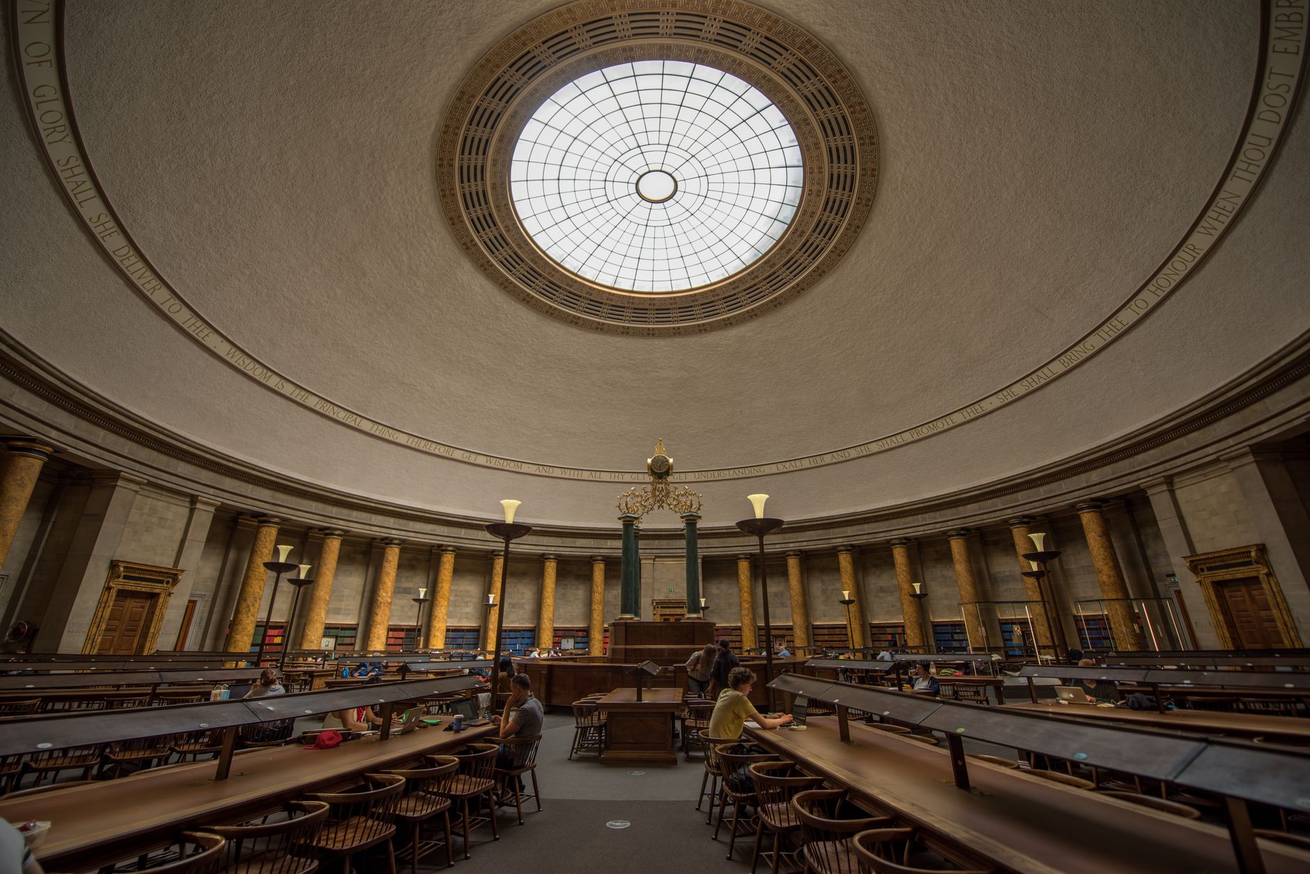 A grand and quiet university library reading room with long tables and tall bookshelves, an ideal environment for autonomous cleaning.