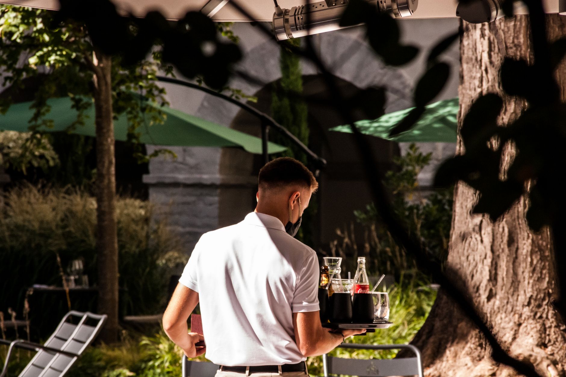 A server carefully carries a heavy tray of food through a crowded restaurant, illustrating the physical tasks that runner robots can automate.