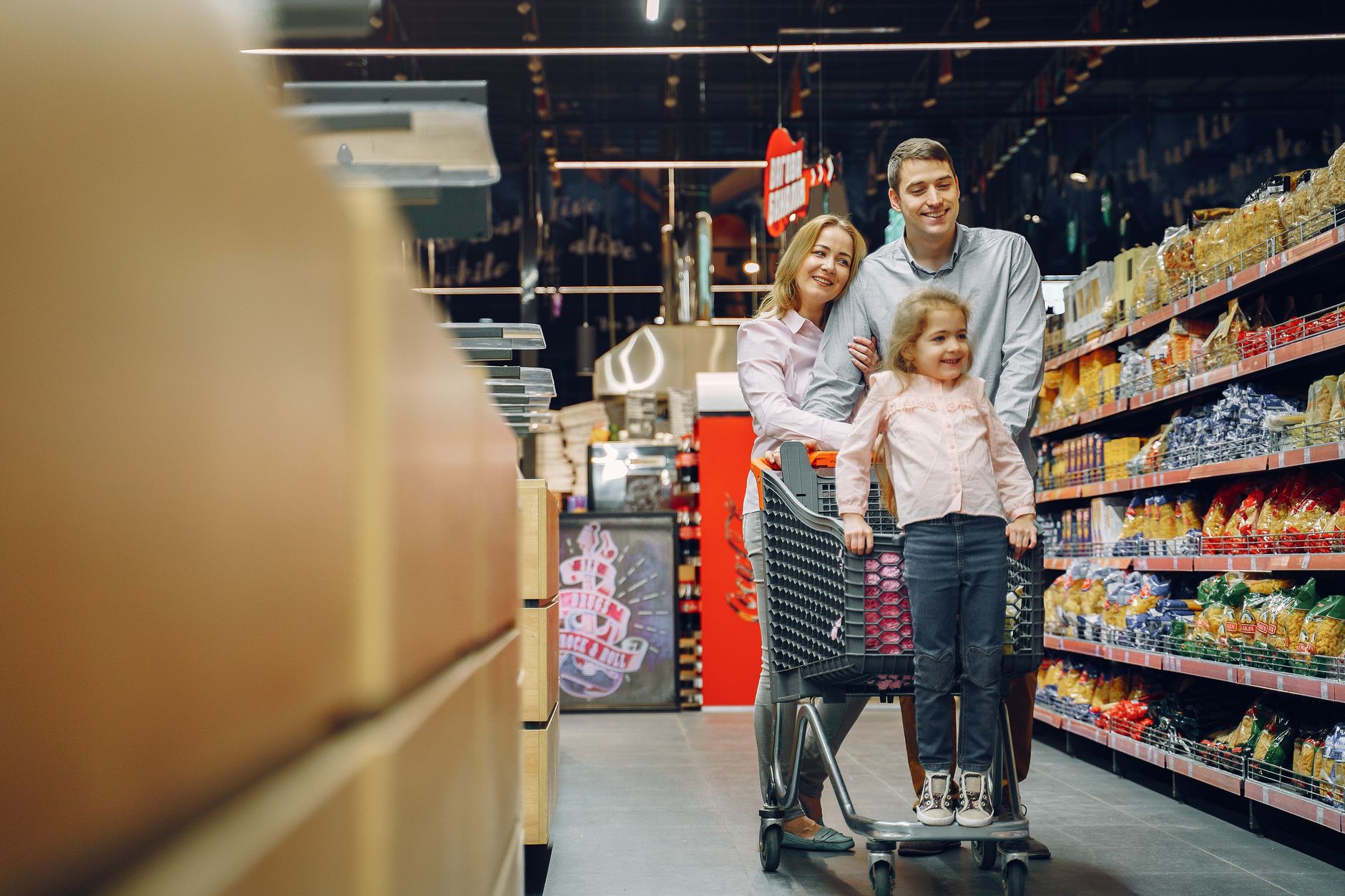 A parent and child happily shopping in the bright, clean aisle of a supermarket, illustrating a positive customer experience.