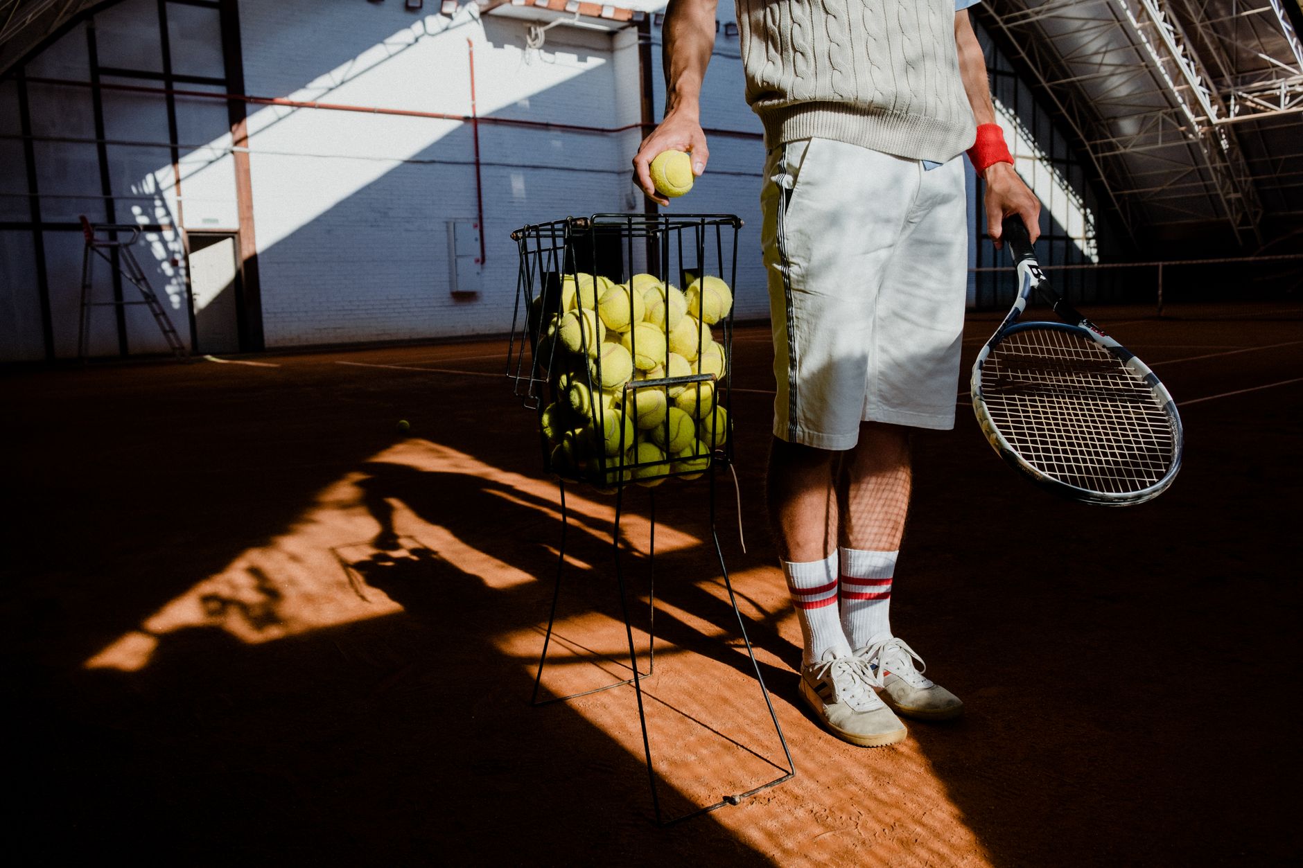 A basket and loose tennis balls rest on a hard court between teaching sessions.