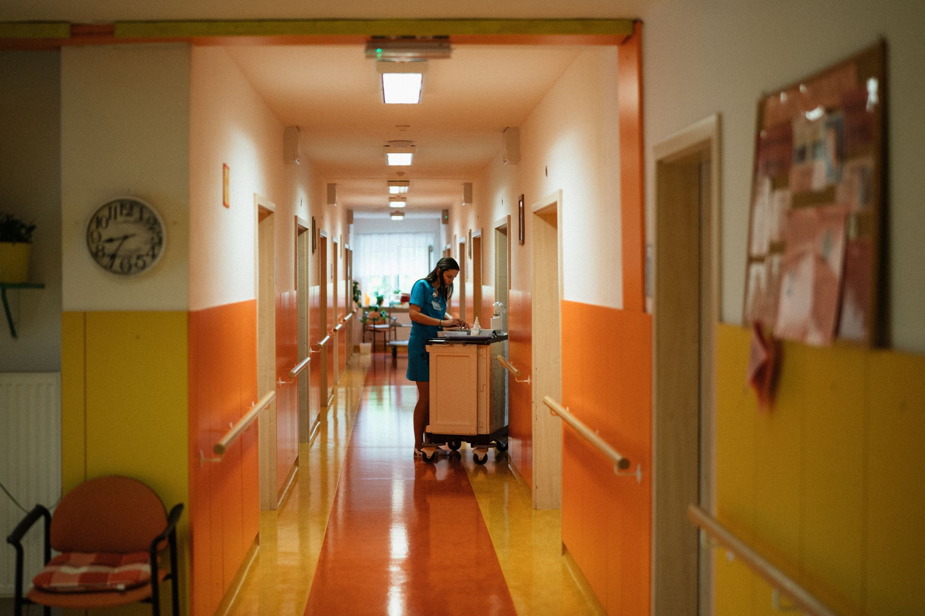 A staff member moving delivery totes through a long institutional corridor, reflecting the repetitive transport loop a campus pilot should relieve first.