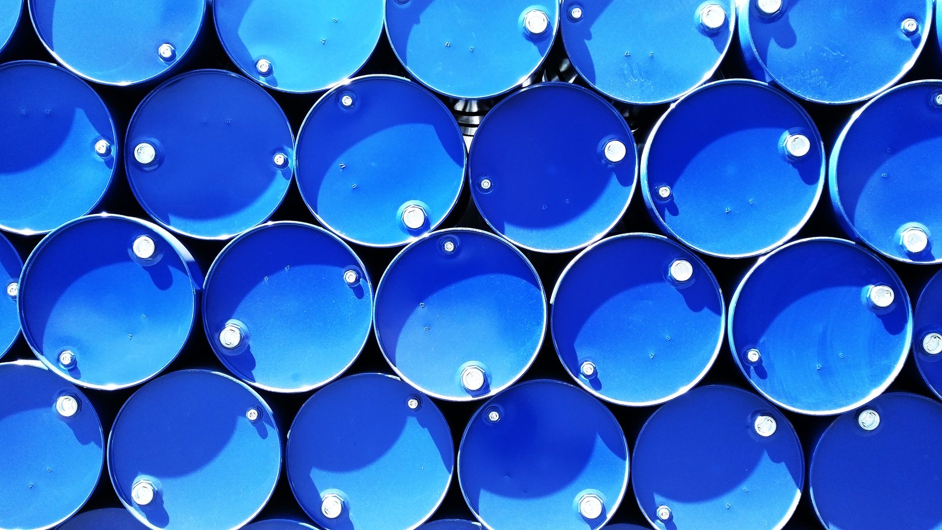 Upright sealed chemical drums stored on spill containment pallets in a plant.
