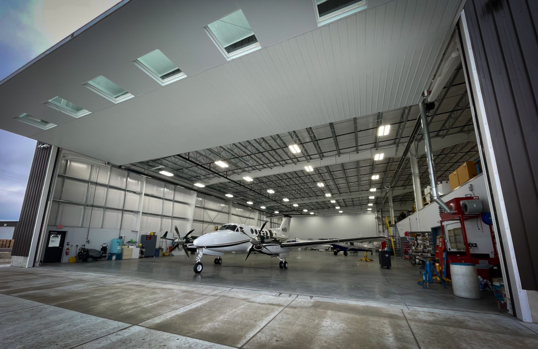 A broad hangar floor with marked walkways, mobile stands, and clear edge routes beside aircraft work areas.