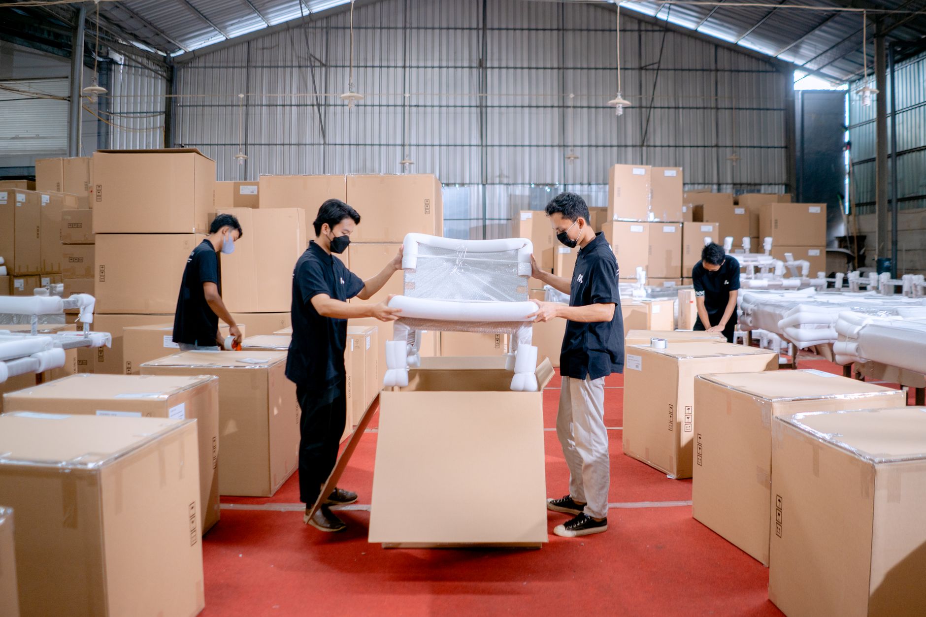 Workers handle furniture components across a busy woodworking production floor.