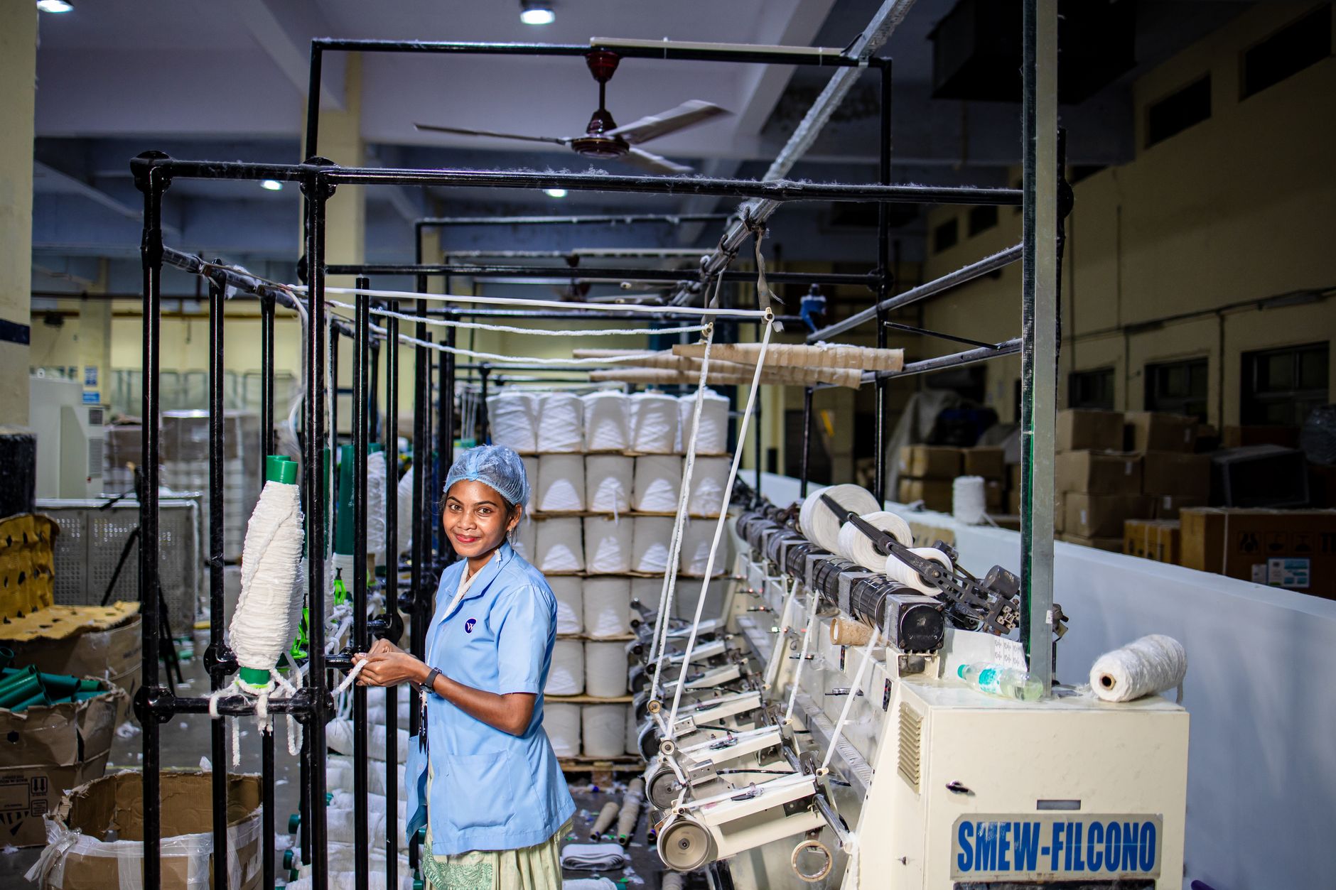A textile worker moving through a long aisle between rows of weaving looms.