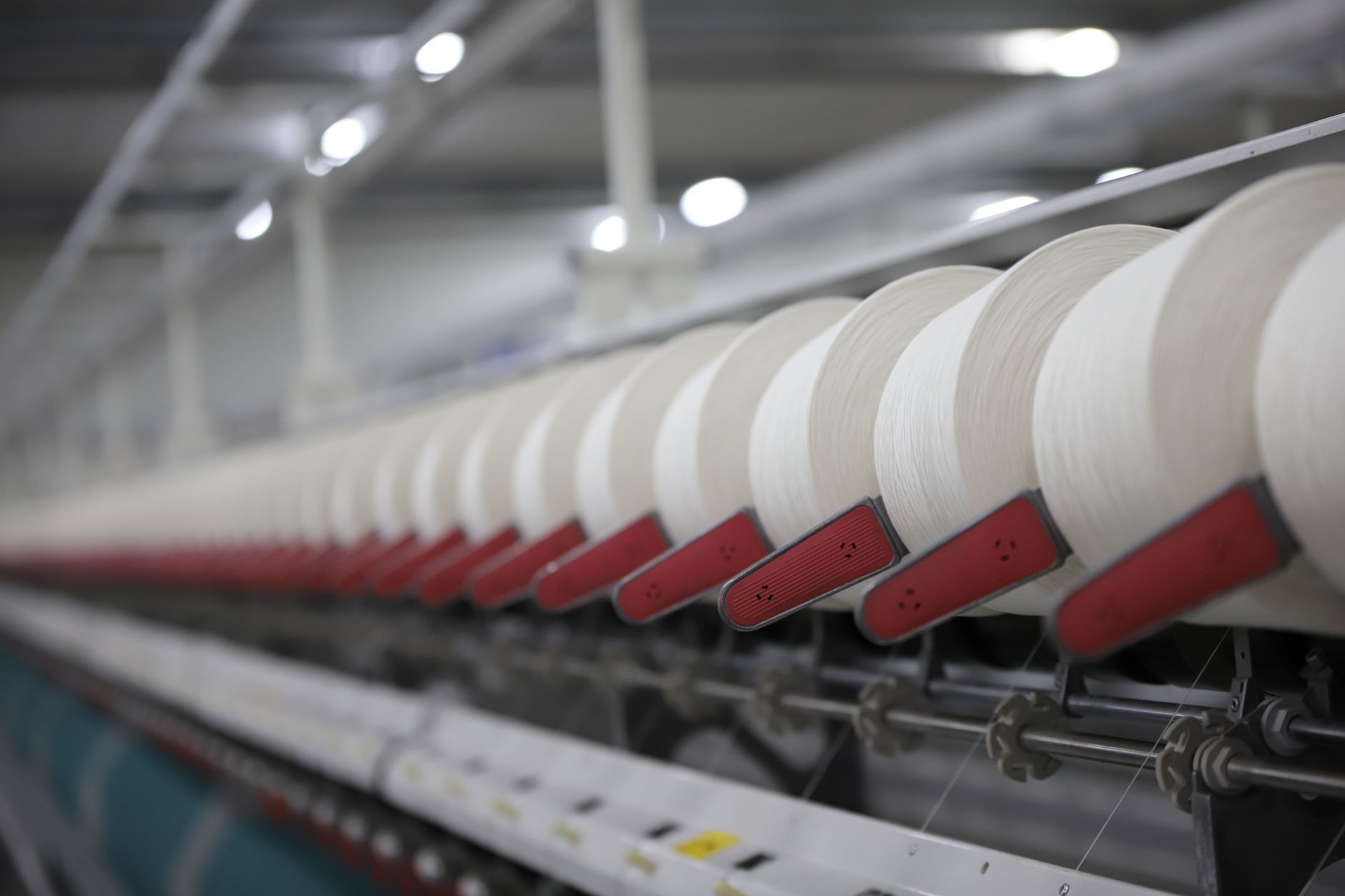 A long textile mill aisle lined with yarn-processing equipment and work-in-process stations.