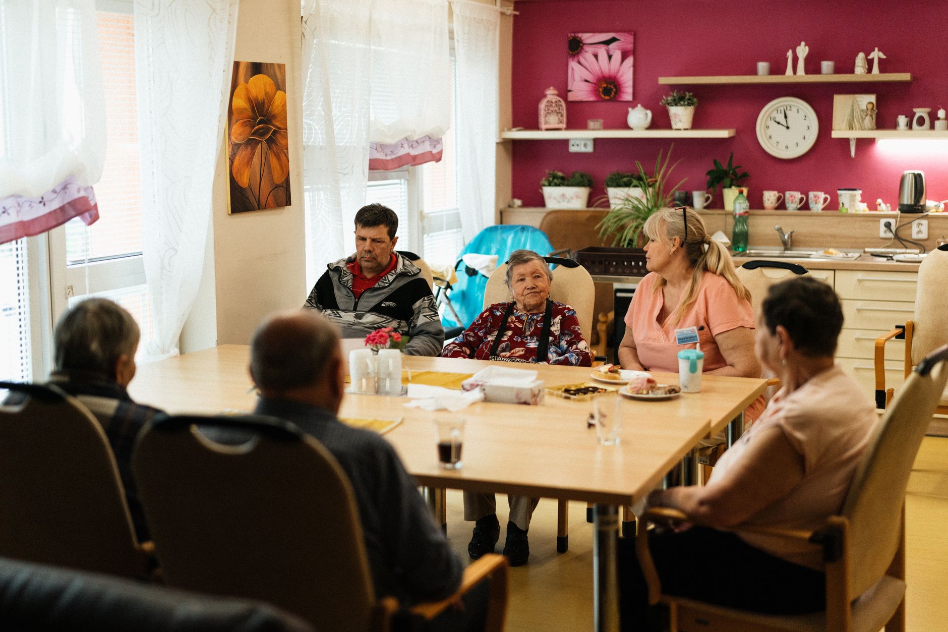 A server chats with residents at their table in a bustling assisted living dining room, illustrating the value of human connection during meals.