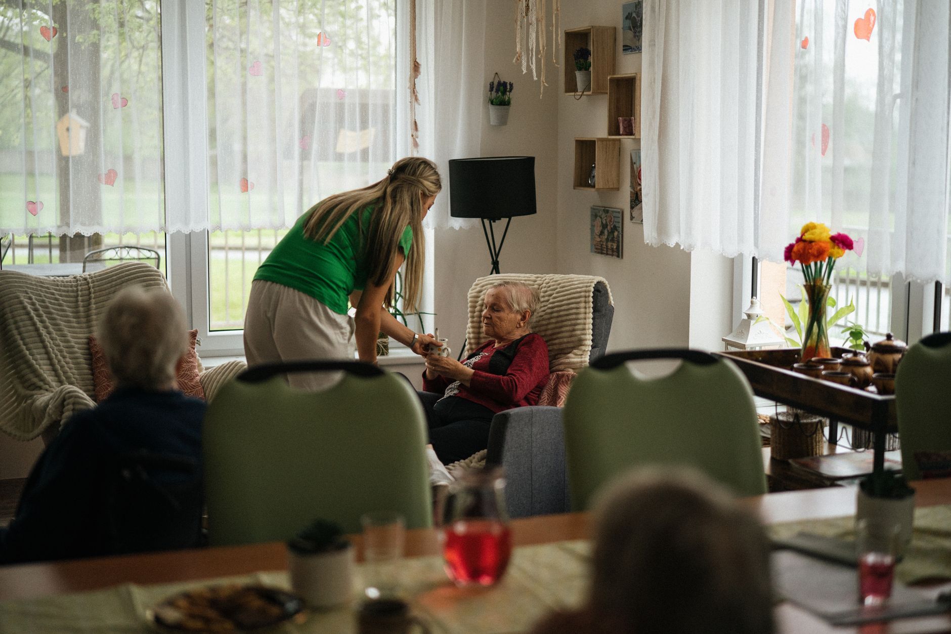 A caregiver sits and talks with a smiling senior resident in a bright, comfortable assisted living community common area.