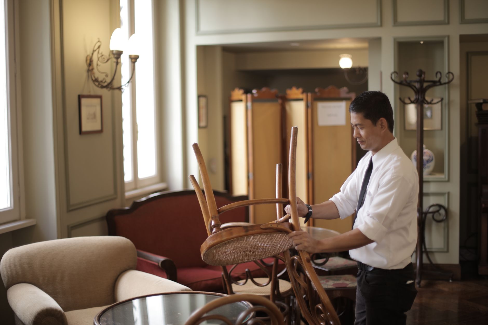 A restaurant server assistant carries a heavy bus tub filled with dirty dishes away from a recently cleared dining table.