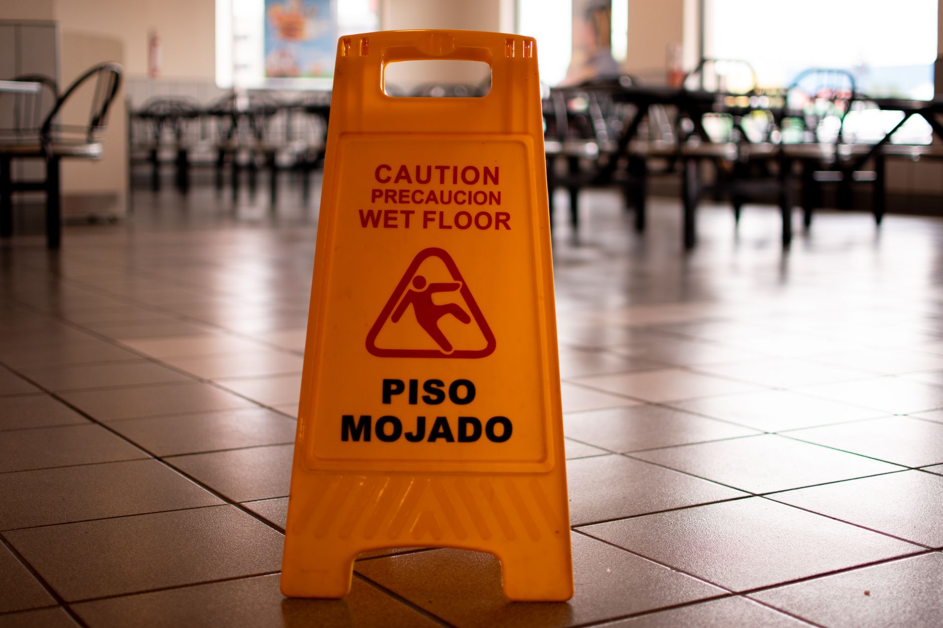 A yellow 'wet floor' sign stands next to a puddle in a tiled hallway, illustrating a slip-and-fall hazard that a robot's recorded footage can document impartially.
