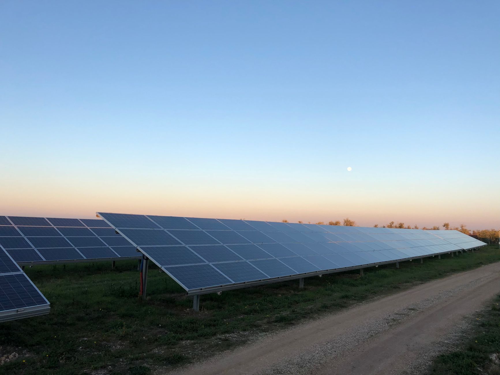 An outdoor security robot patrols the perimeter of a large, modern solar farm at twilight.
