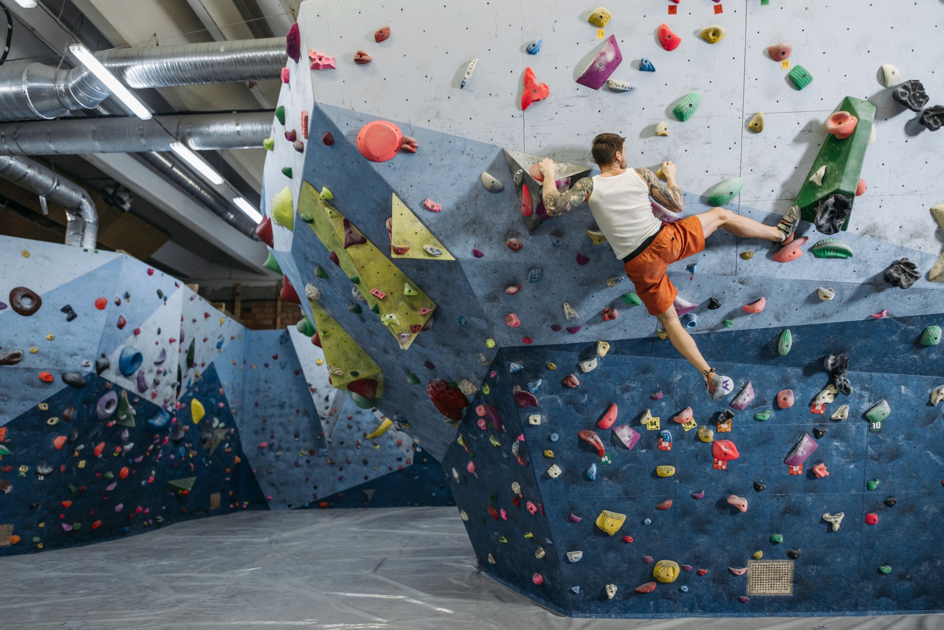Wide view of an indoor climbing gym with tall walls, rubber flooring, and circulation aisles that frame the floor conditions a buyer has to evaluate.