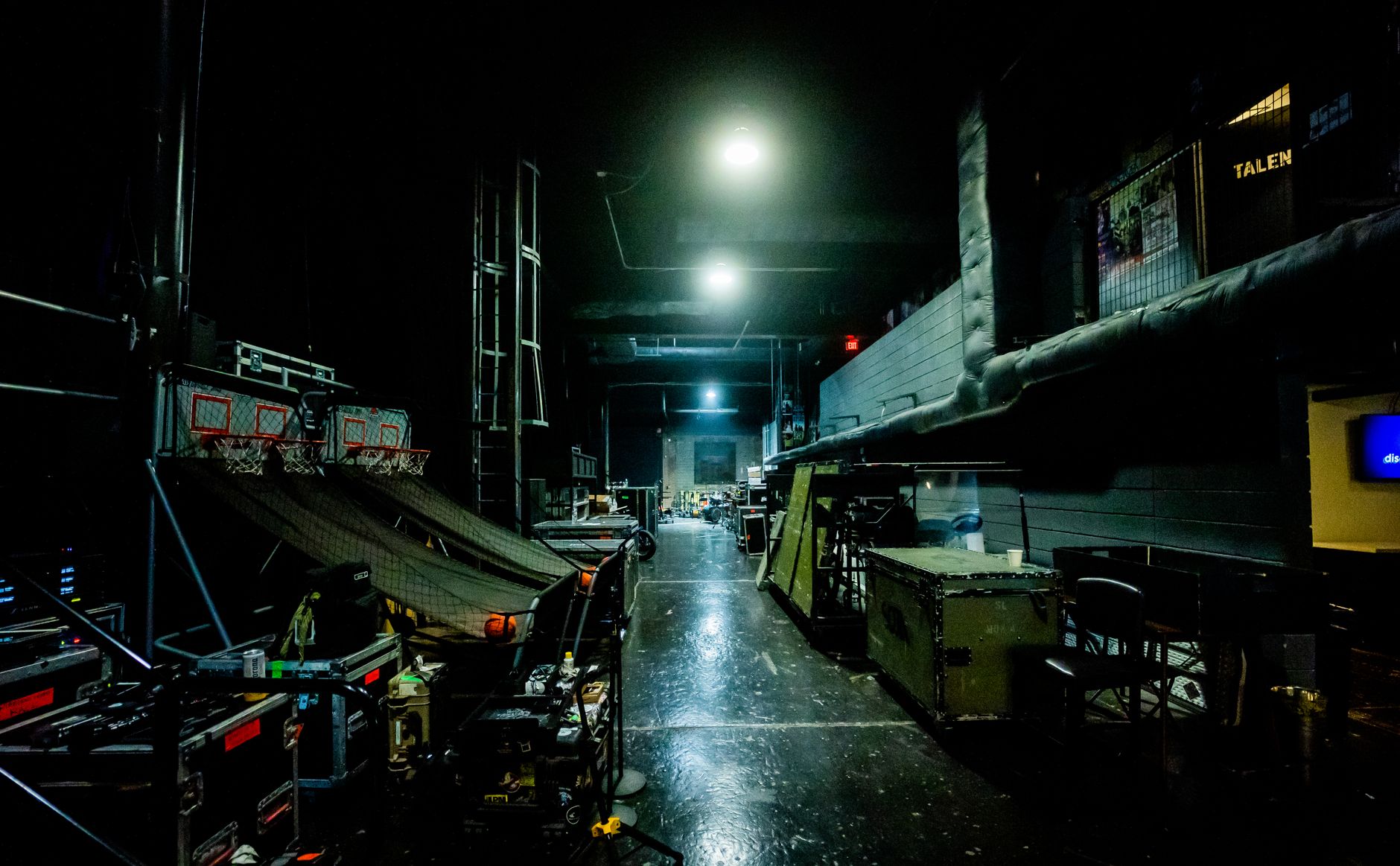 A narrow backstage corridor with doorways, equipment cases and limited maneuvering space.