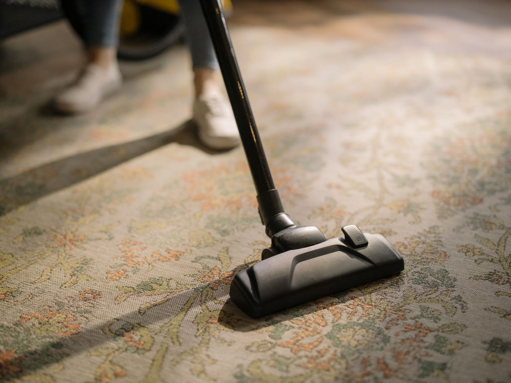 A worker vacuuming along a carpet edge, showing the detailed border cleaning that still needs human follow-up in an arcade or family entertainment center.