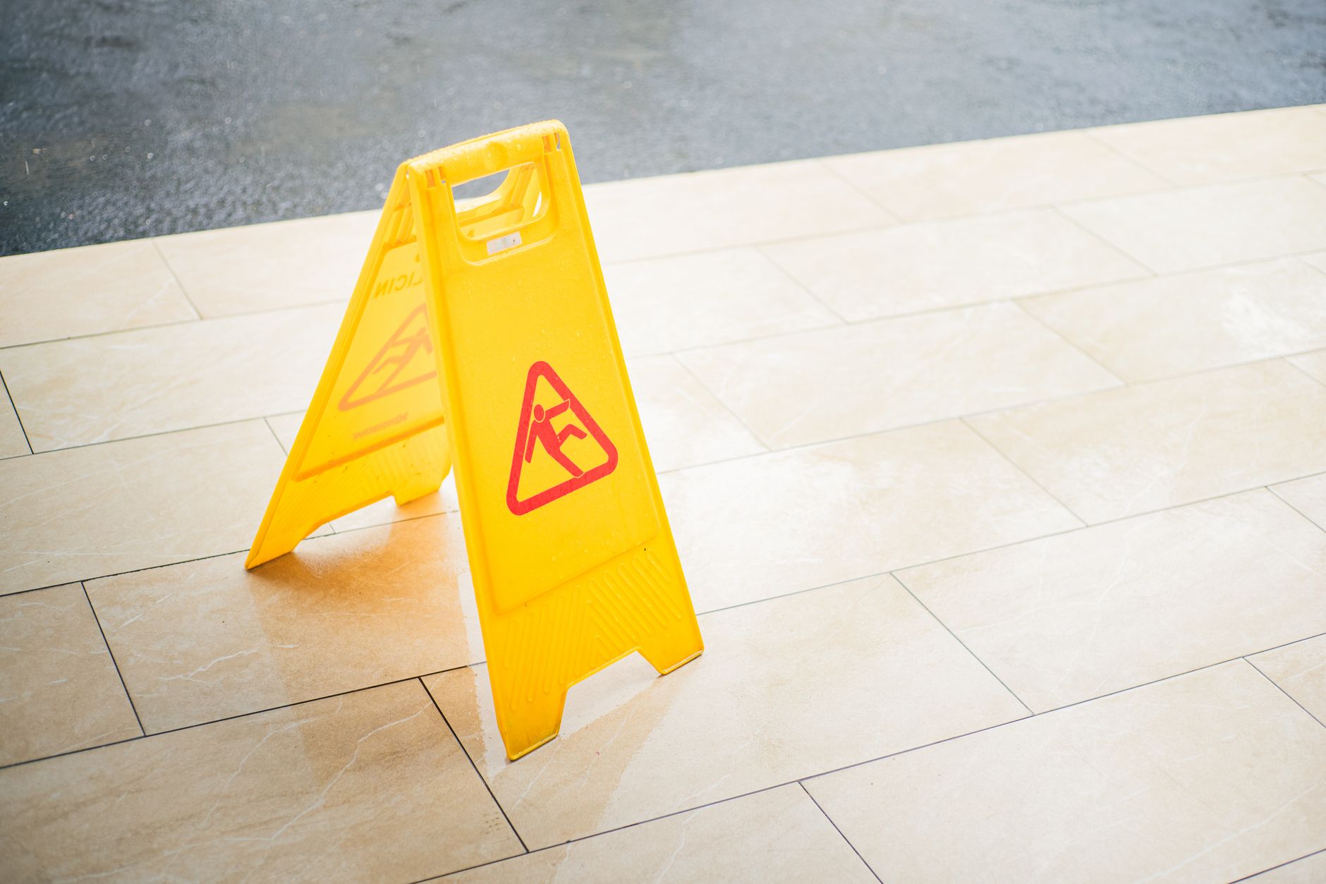 A wet-floor warning and recently cleaned hard floor in a commercial restroom-adjacent area, underscoring spill response and slip risk.