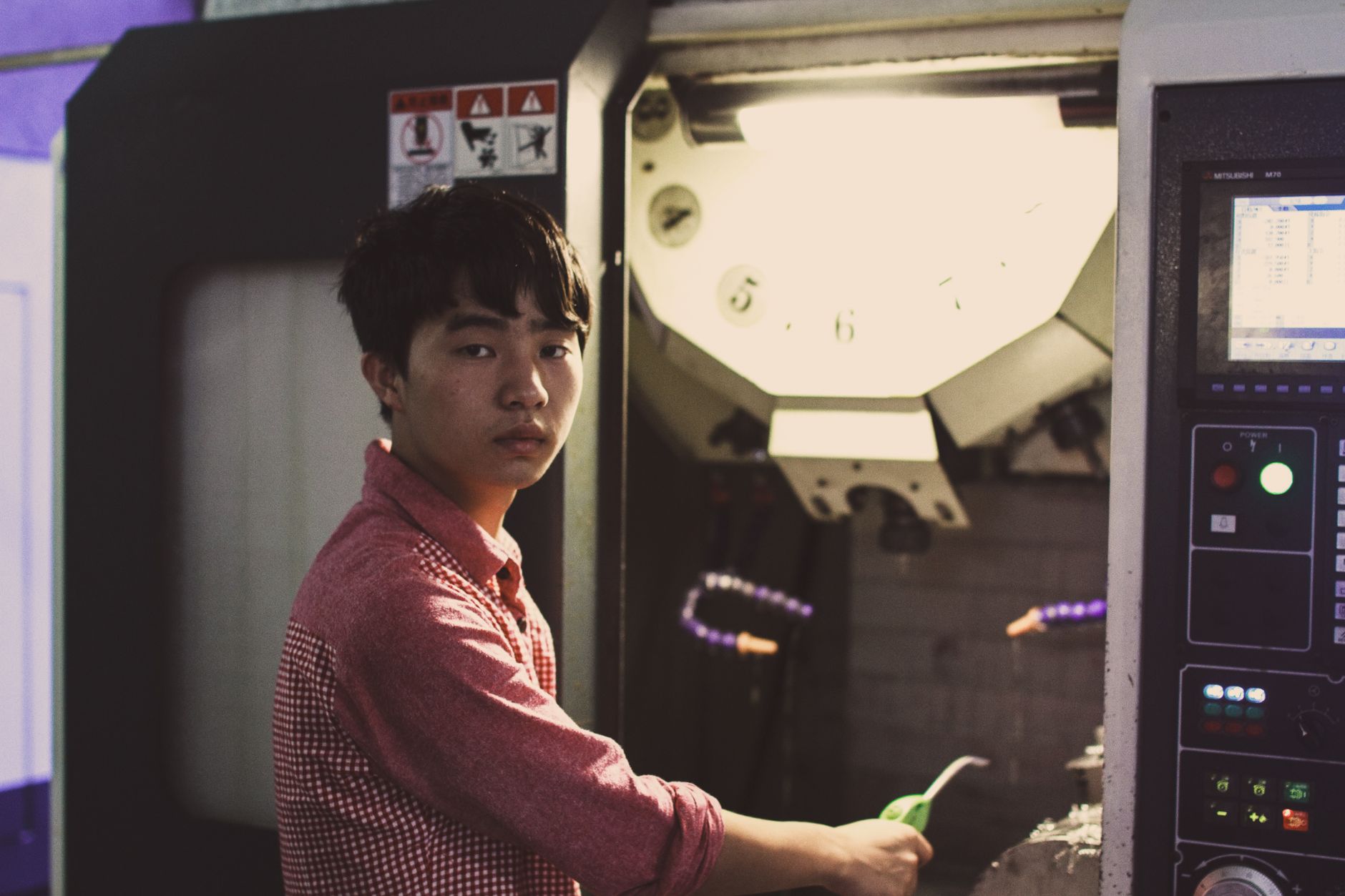 A skilled manufacturing technician monitors a complex piece of industrial equipment from a control panel, representing the technical expertise needed in modern factories.