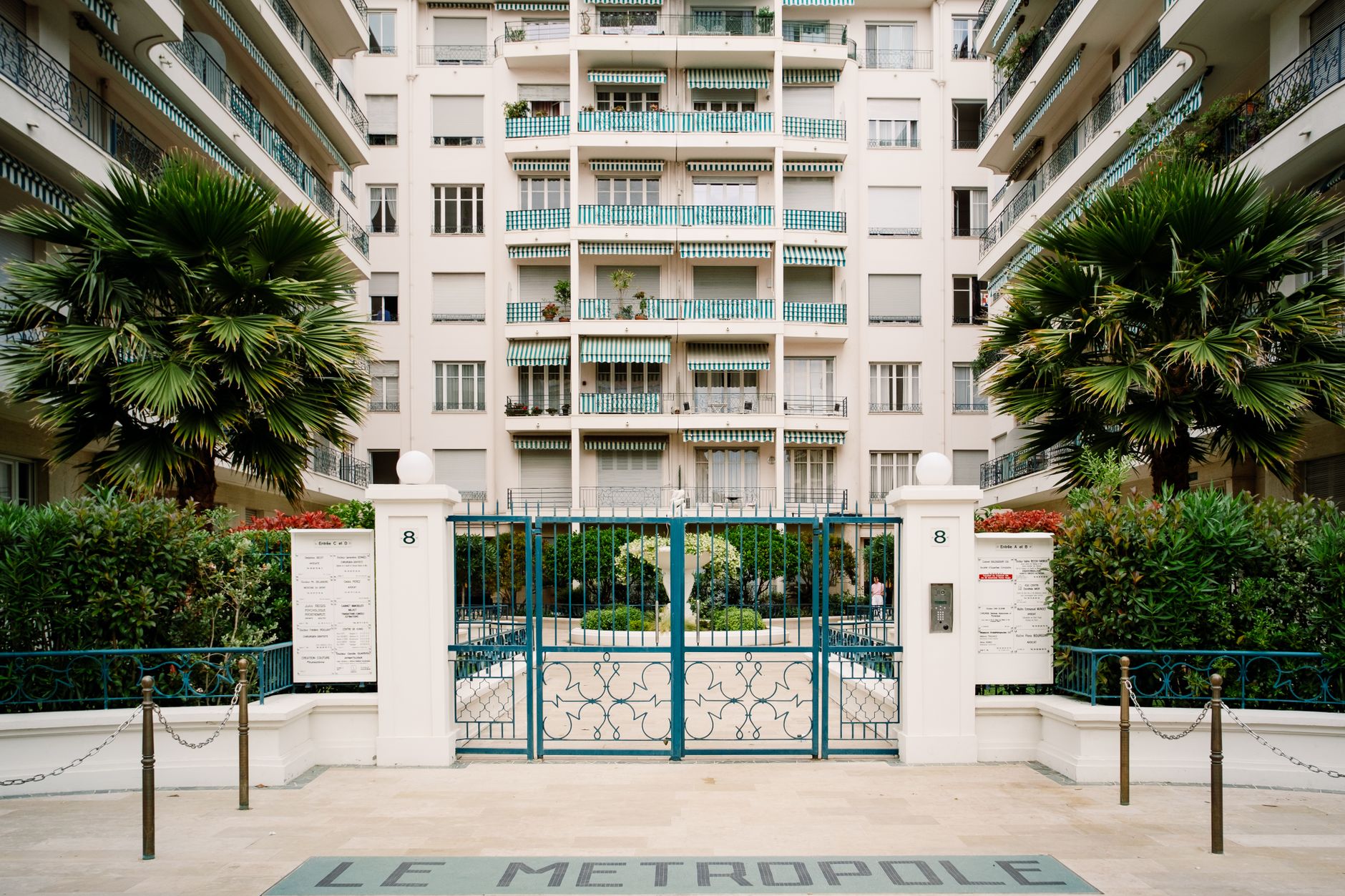 A gated apartment entrance with a vehicle lane, access point, and surrounding residential buildings.