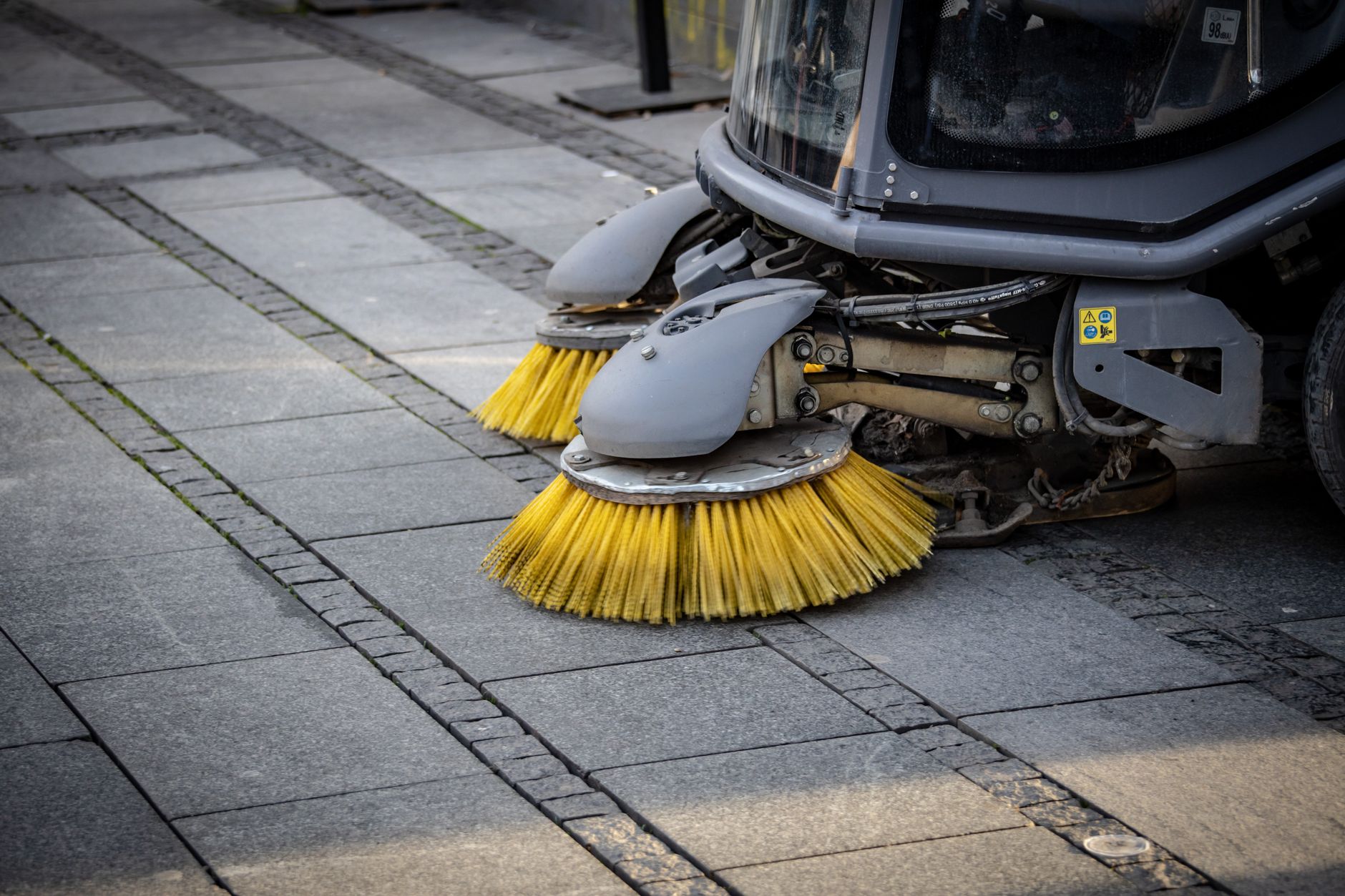 Compact sweeper cleaning a paved outdoor path