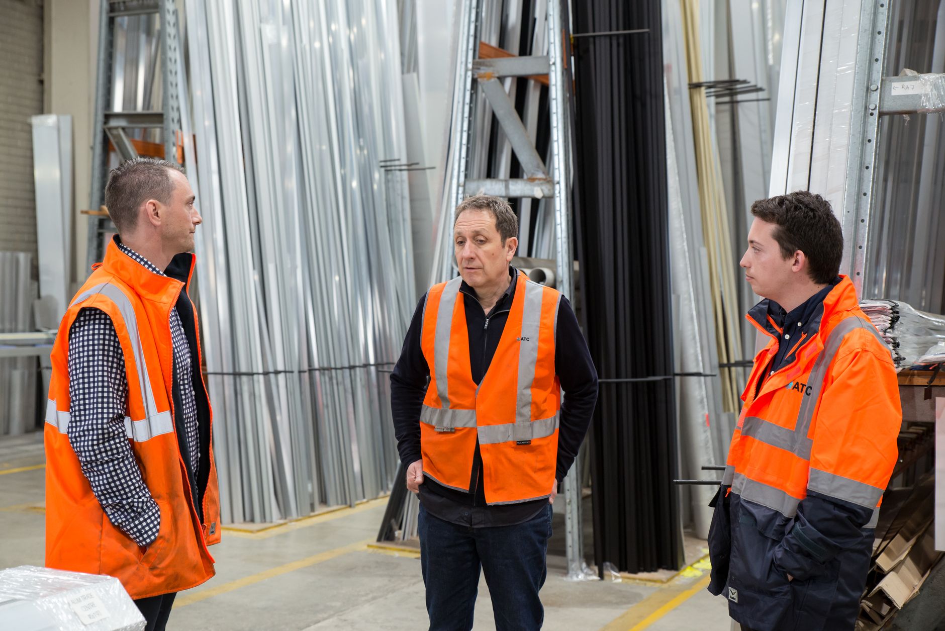 An engaged group of warehouse workers, including a manager, having a positive discussion in an aisle surrounded by inventory.