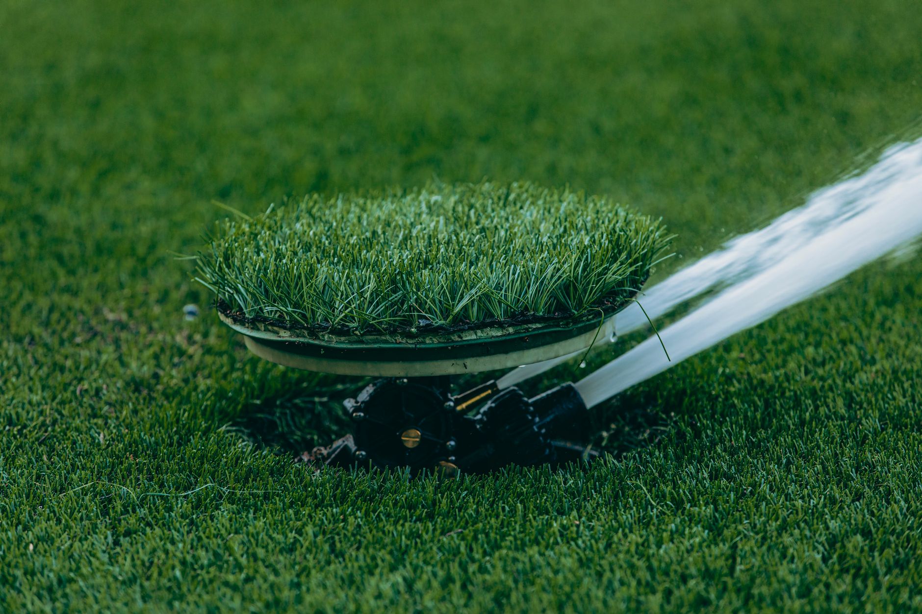 Sprinklers watering turf beside a maintained grass strip on a large grounds site.