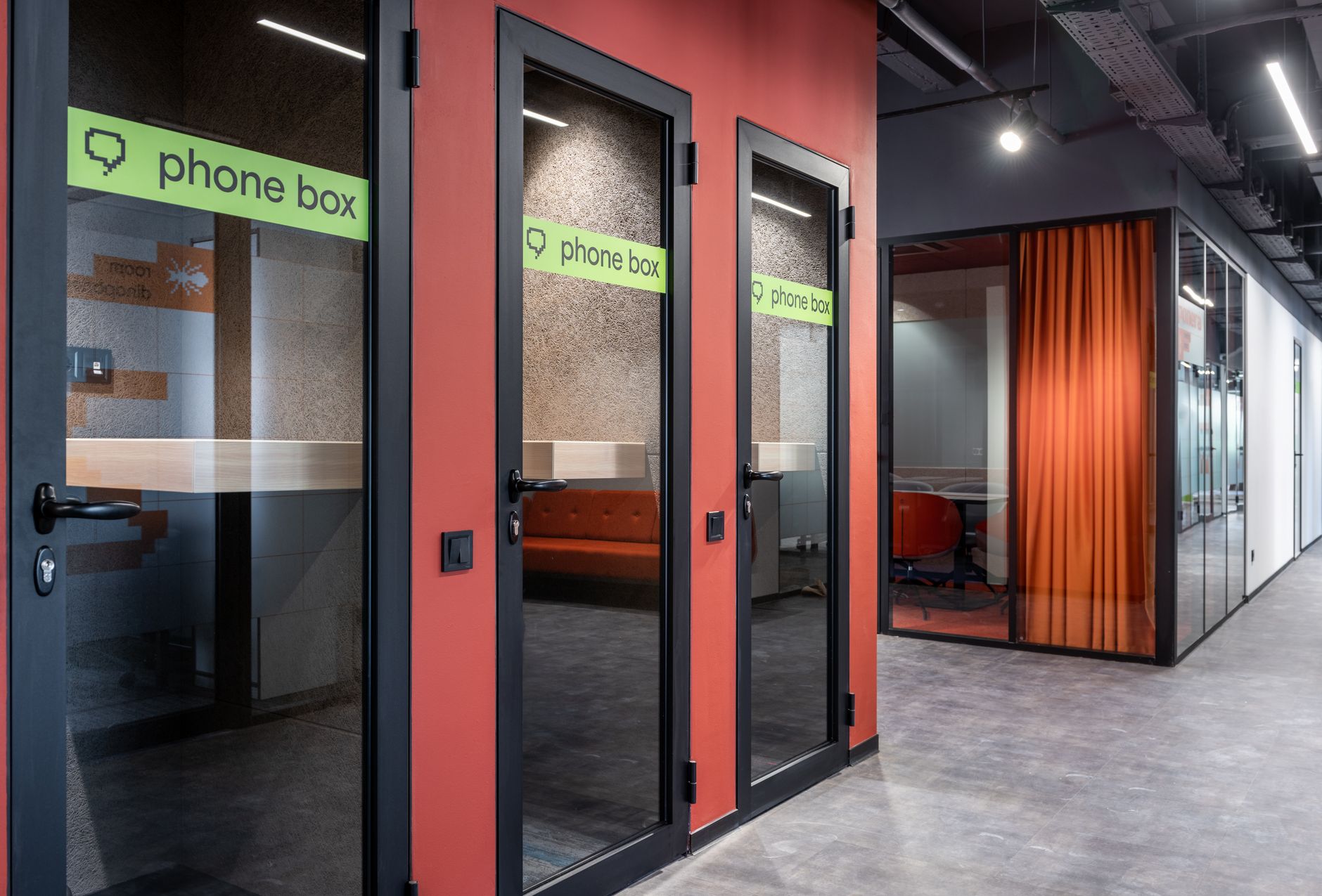 A coworking corridor lined with phone booths and furniture creating several narrow circulation points.