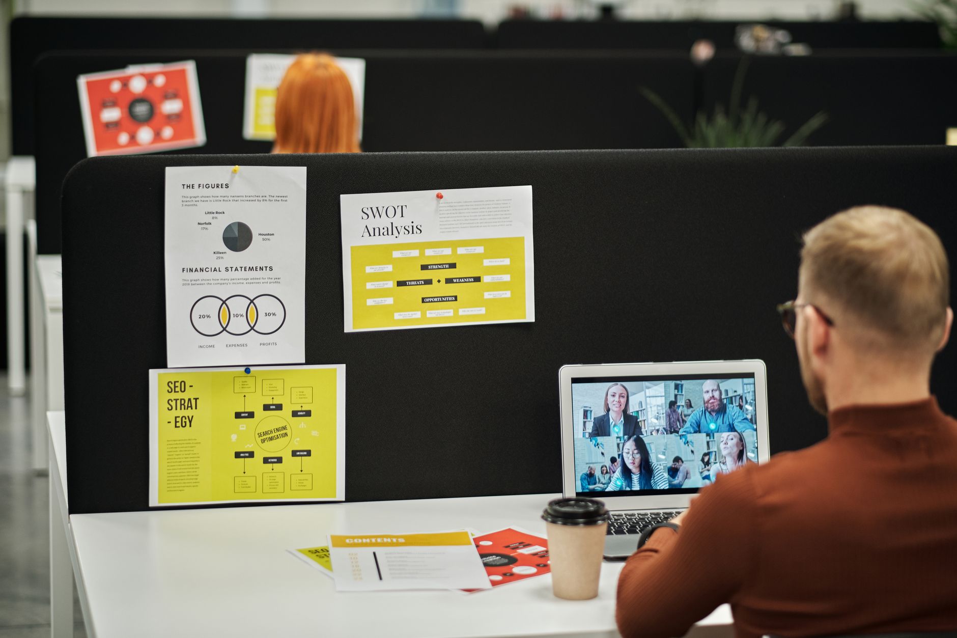 A member taking a video call at a desk in a busy open-plan coworking area.