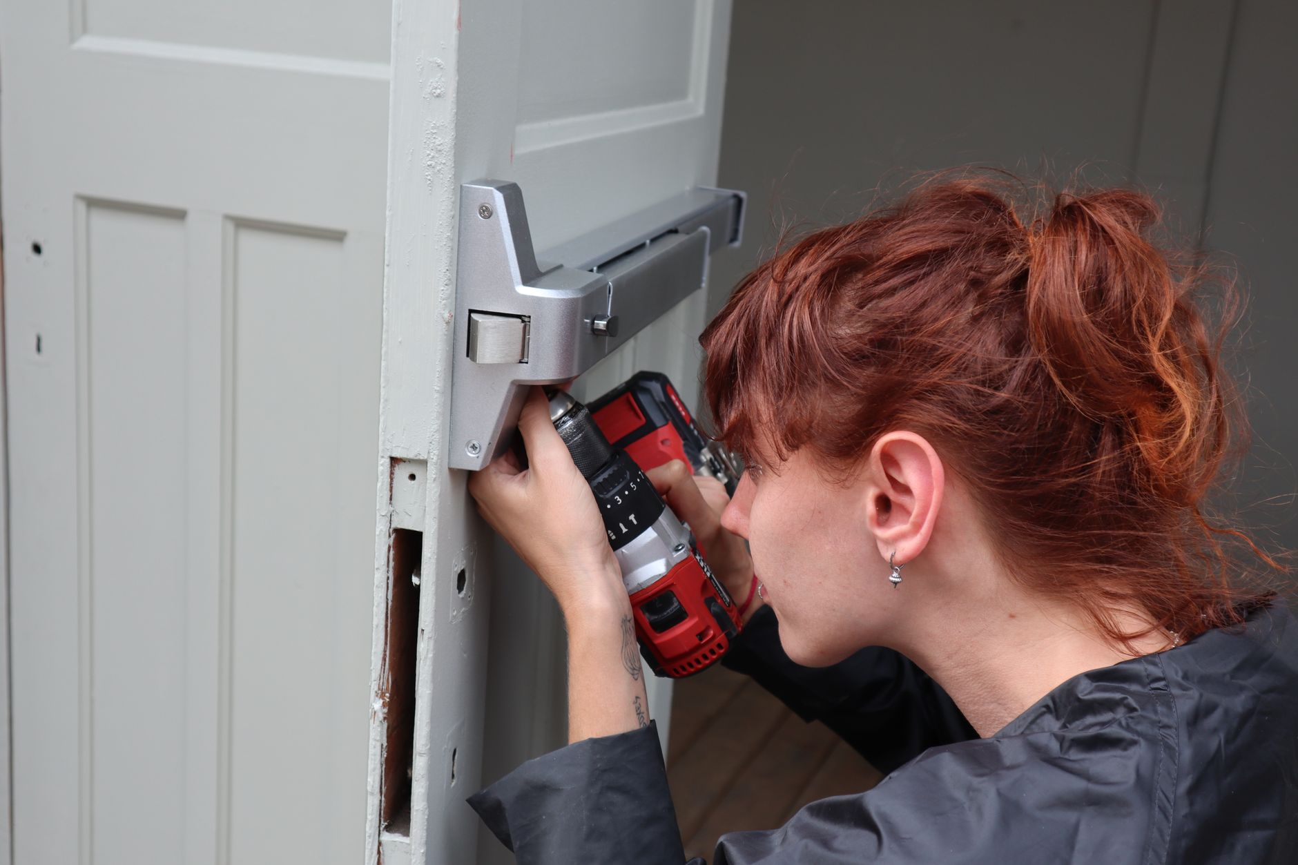 A worker installs hardware on a frame with a powered screwdriver, illustrating the fastening details a cobot cell must control.