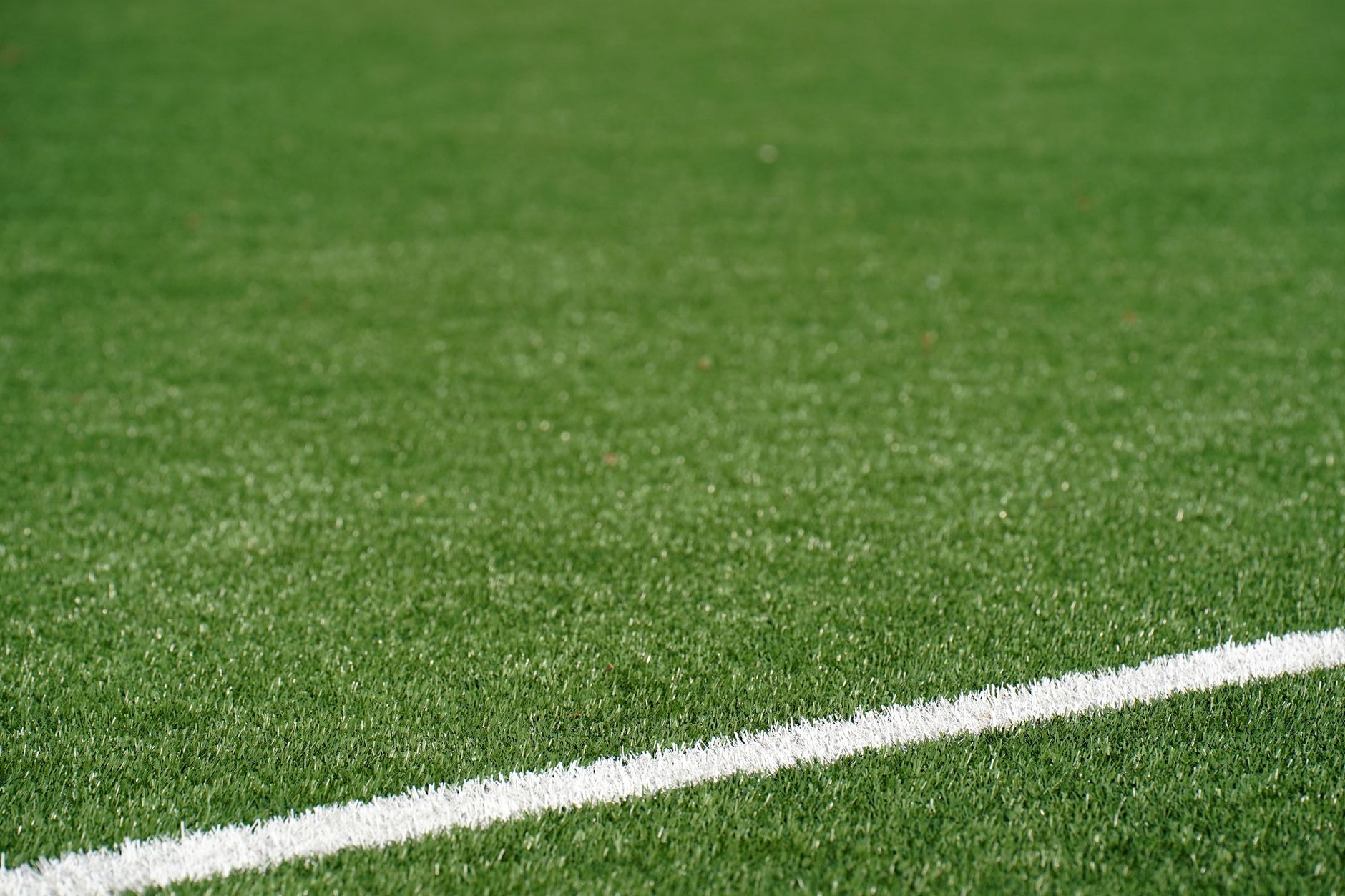 Close-up of synthetic turf fibers rising above dark infill granules, the detail that determines whether a cleaning head will skim or dig.
