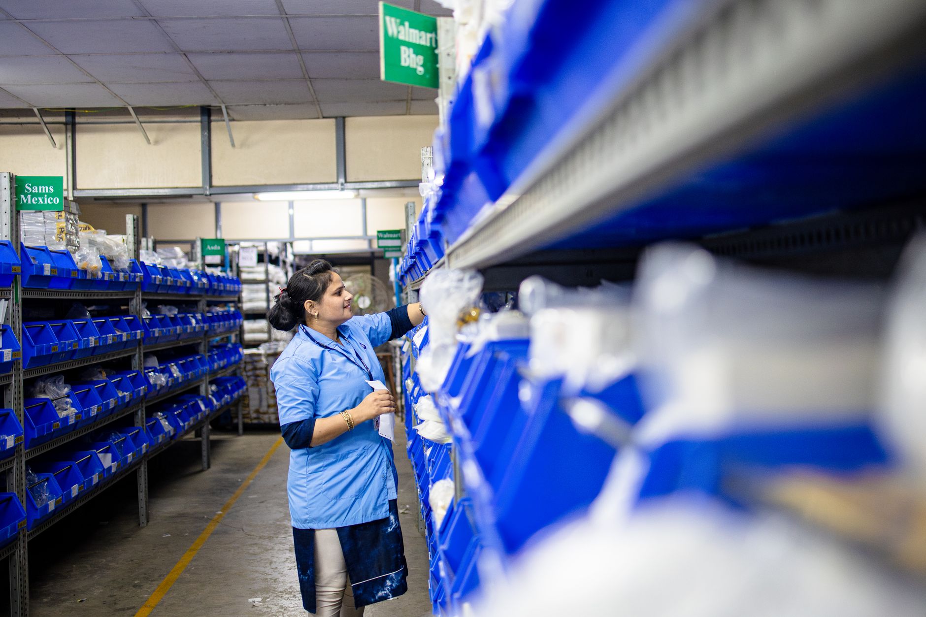 A warehouse worker handling parts totes beside organized storage shelves.