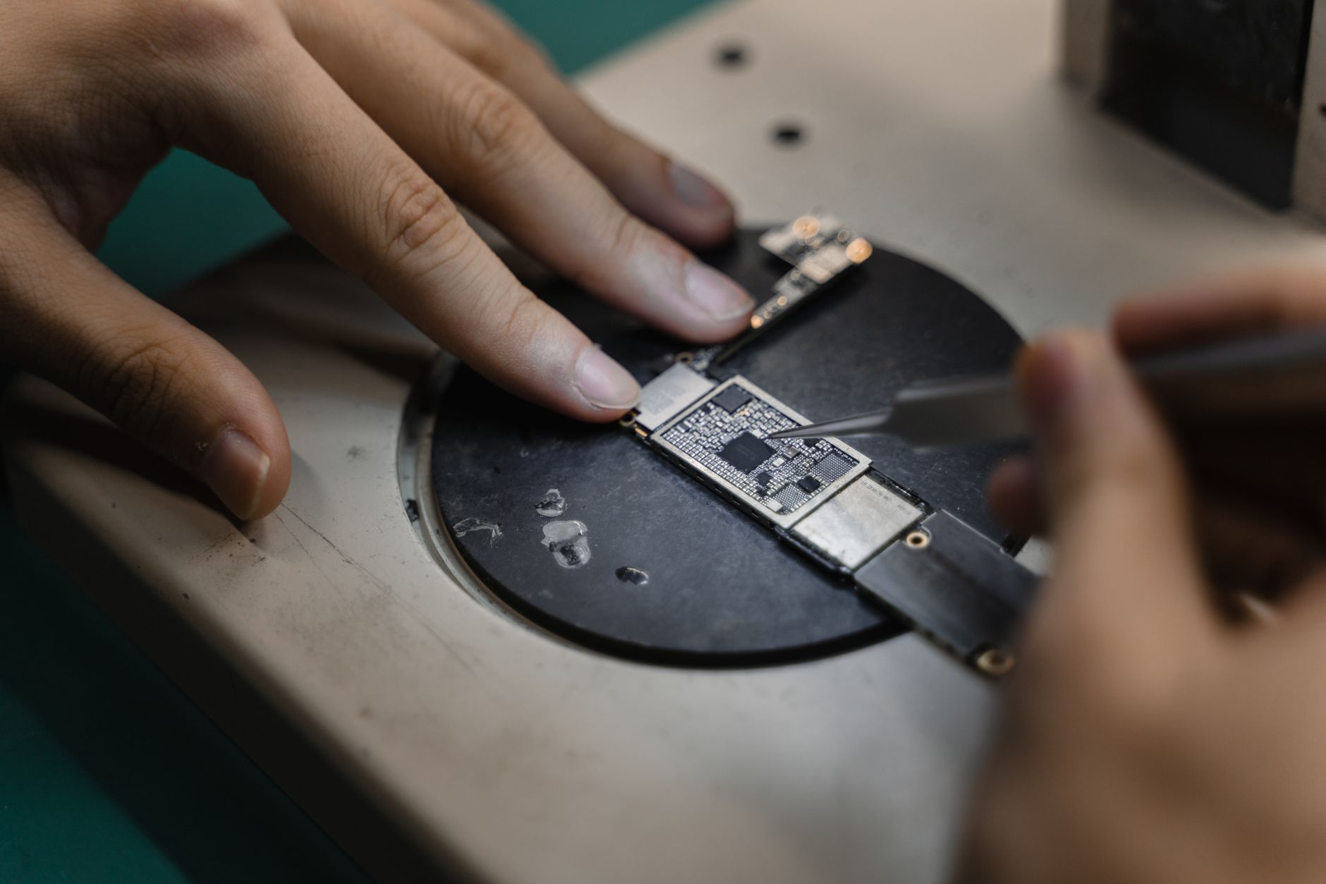 Gloved hands carefully handle a circuit board on an electronics workbench.