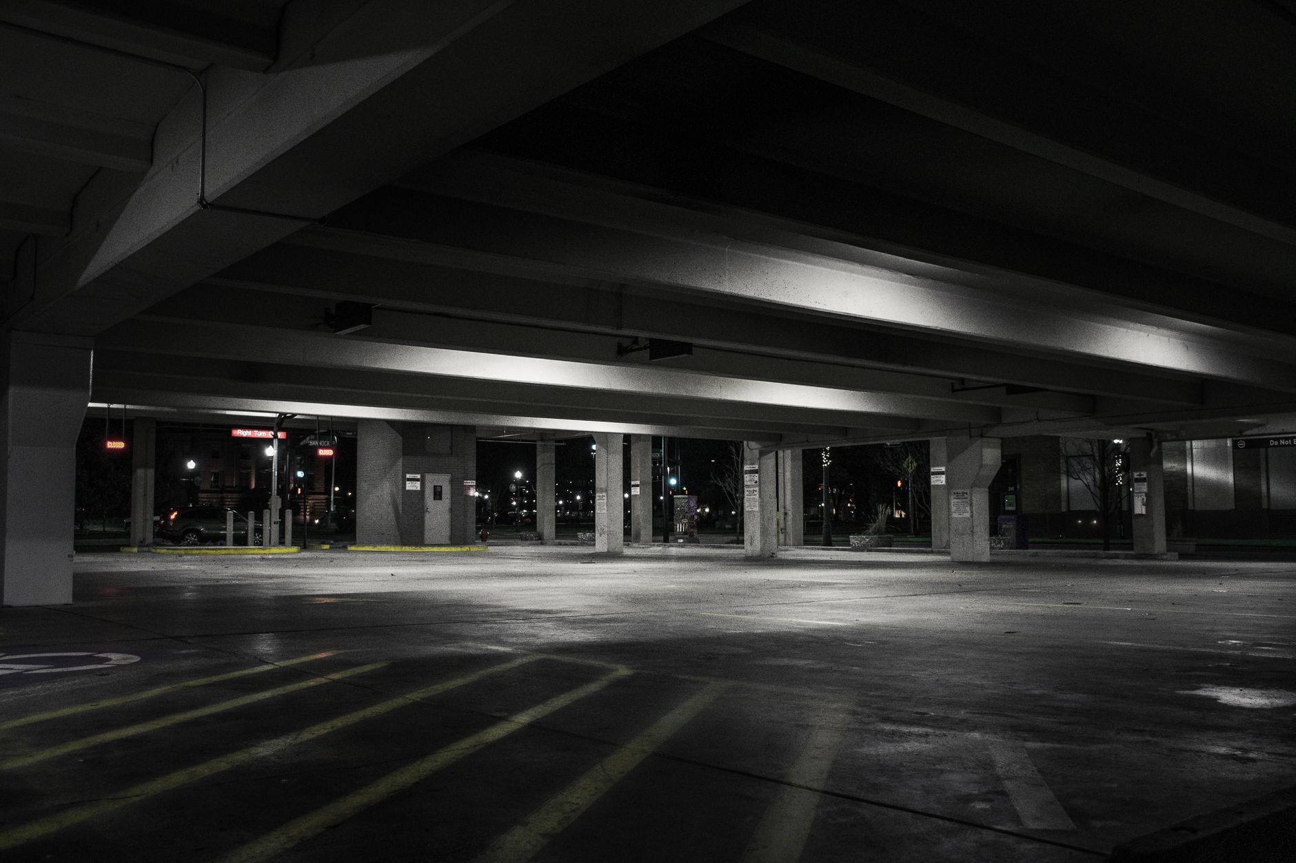 An empty level of a parking garage at night, where pools of light are contrasted with deep shadows in the corners, highlighting potential security risks.