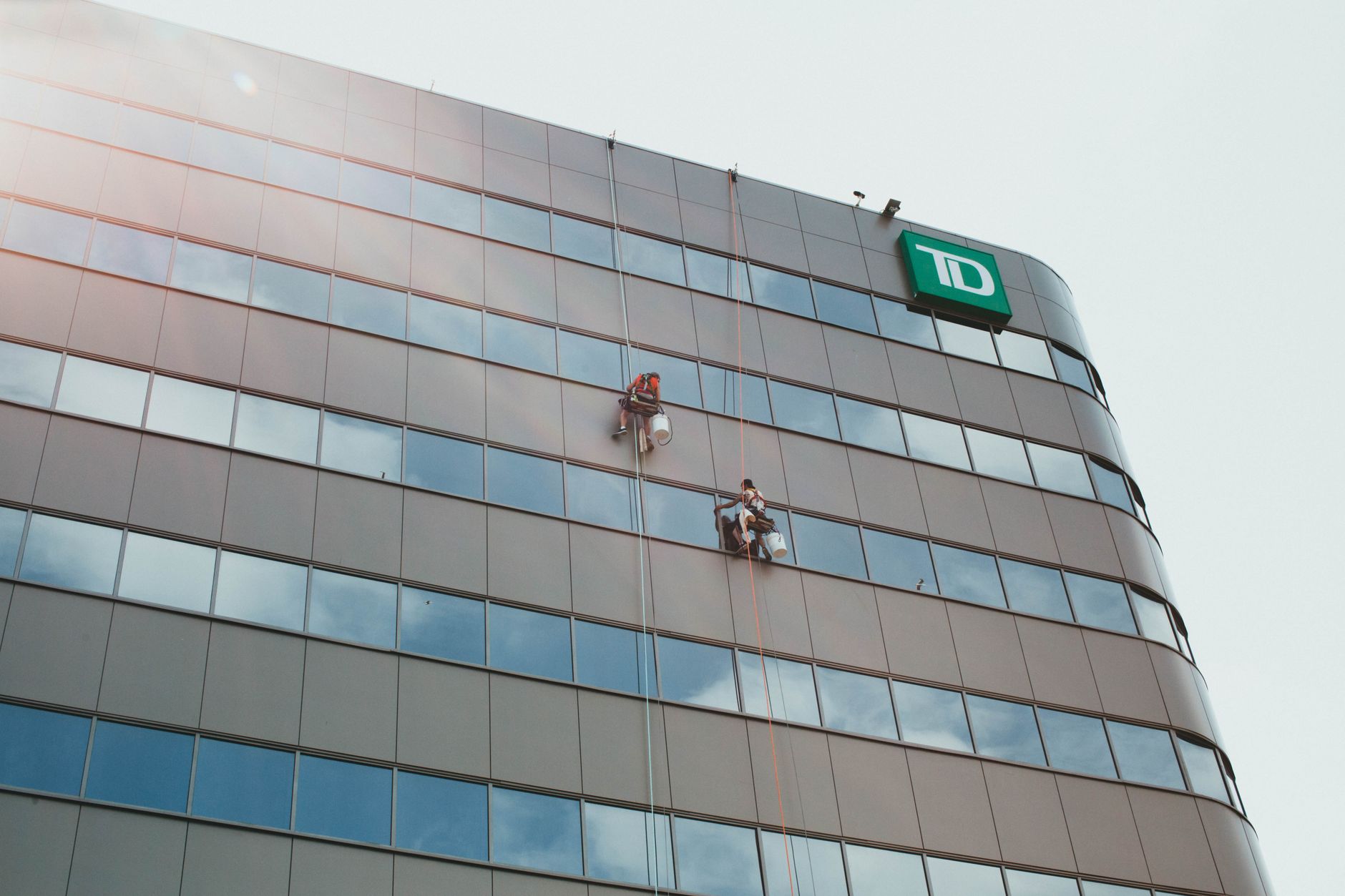 A view from above of a window washer's scaffolding rig high on the side of a glass skyscraper, illustrating a dangerous exterior maintenance job.