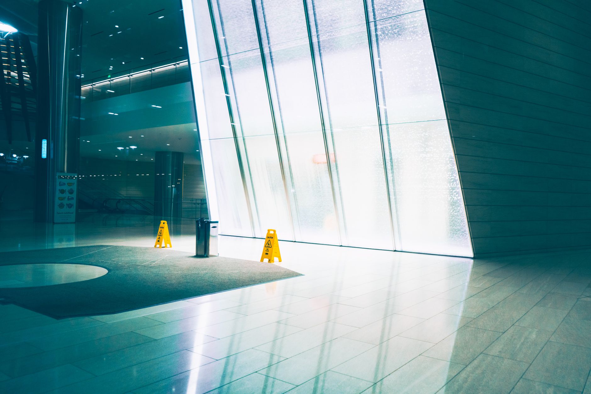 Moisture collects on a commercial lobby floor near the entrance during wet weather, illustrating why immediate spill response matters in high-traffic spaces.