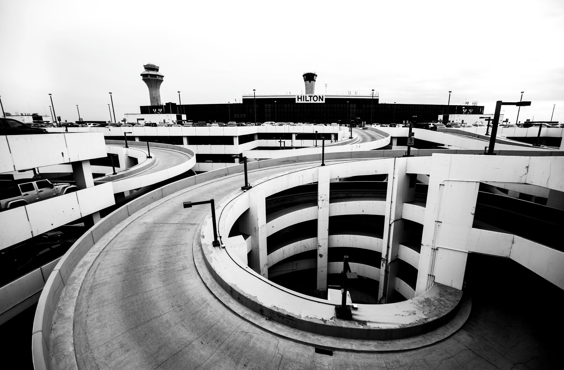 Covered airport rental-car lanes with parked vehicles, bright overhead lighting, and clear customer walk zones.