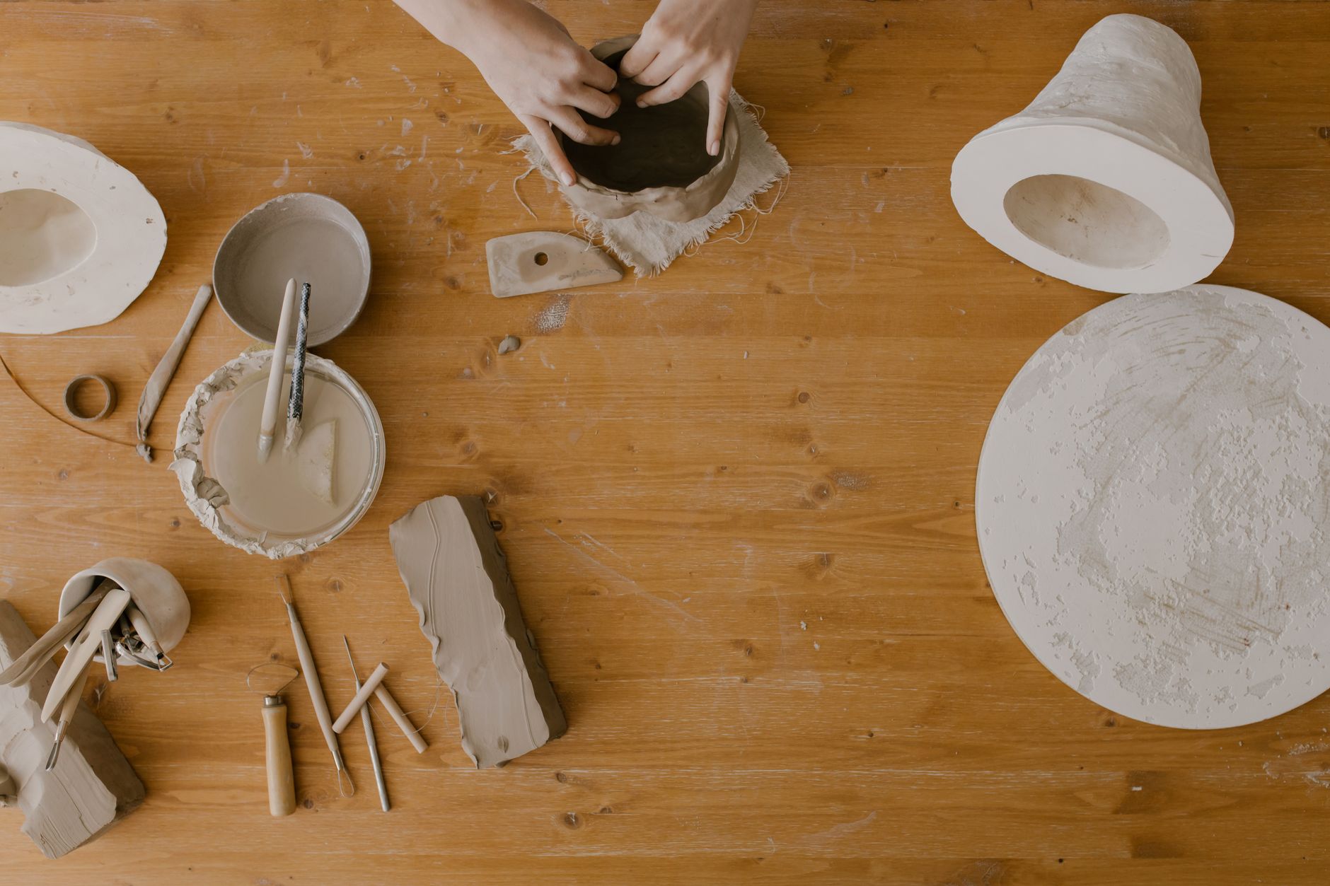 Students work at pottery wheels in a bright studio with hard floors and shelving for clay tools.