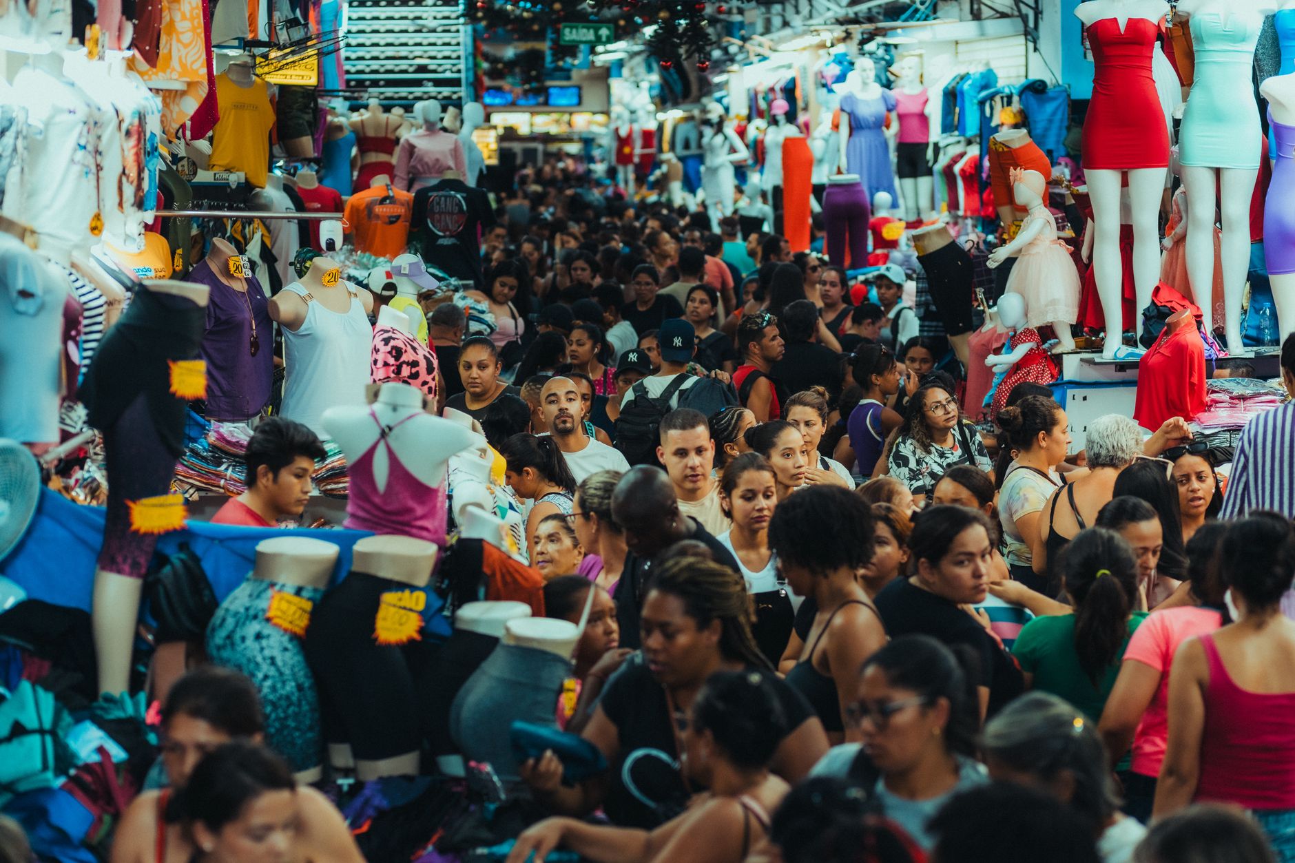 Shoppers, strollers, and vendor displays sharing a crowded indoor market aisle during open hours.