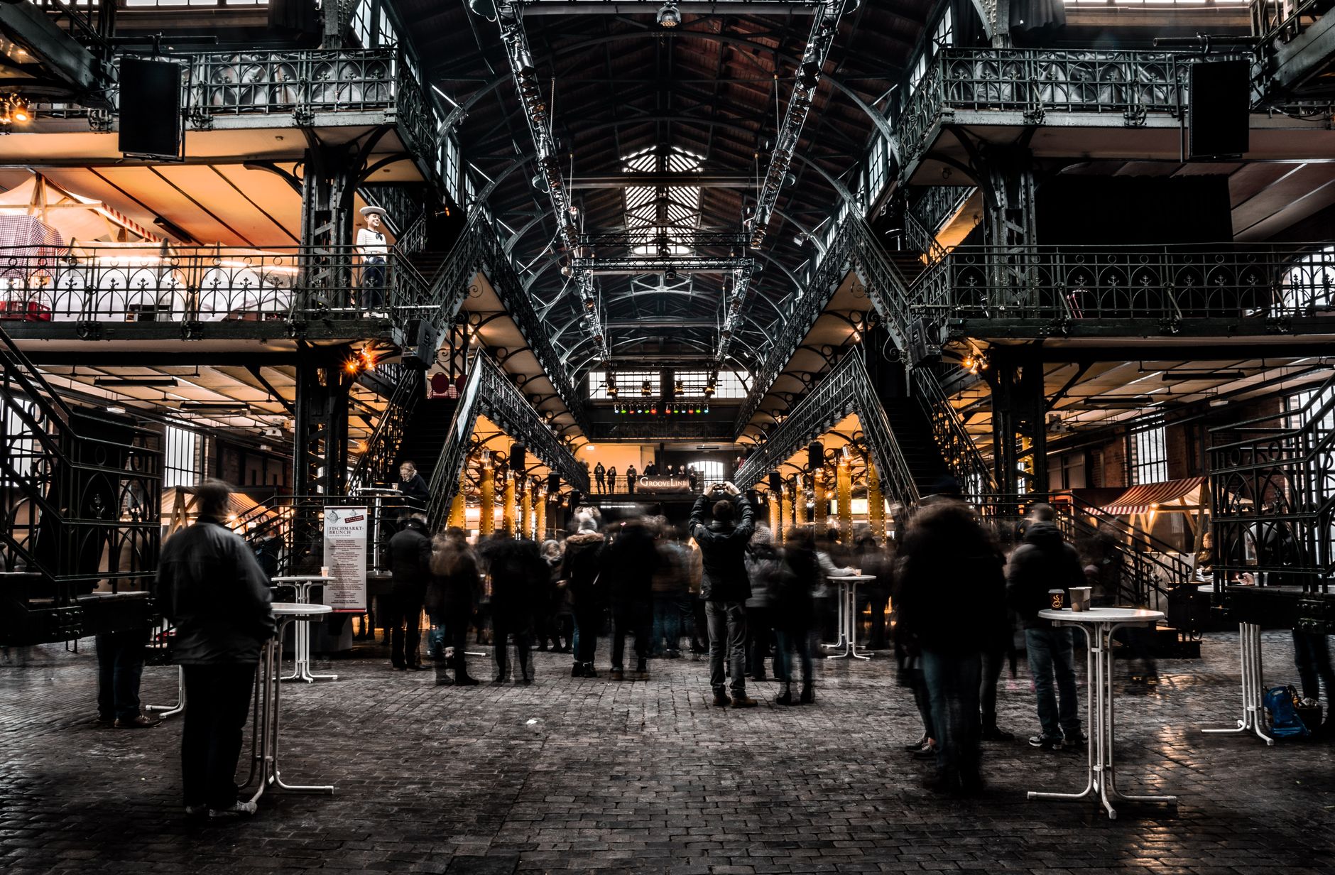 A broad aisle inside a busy indoor public market with shoppers moving between food stalls.