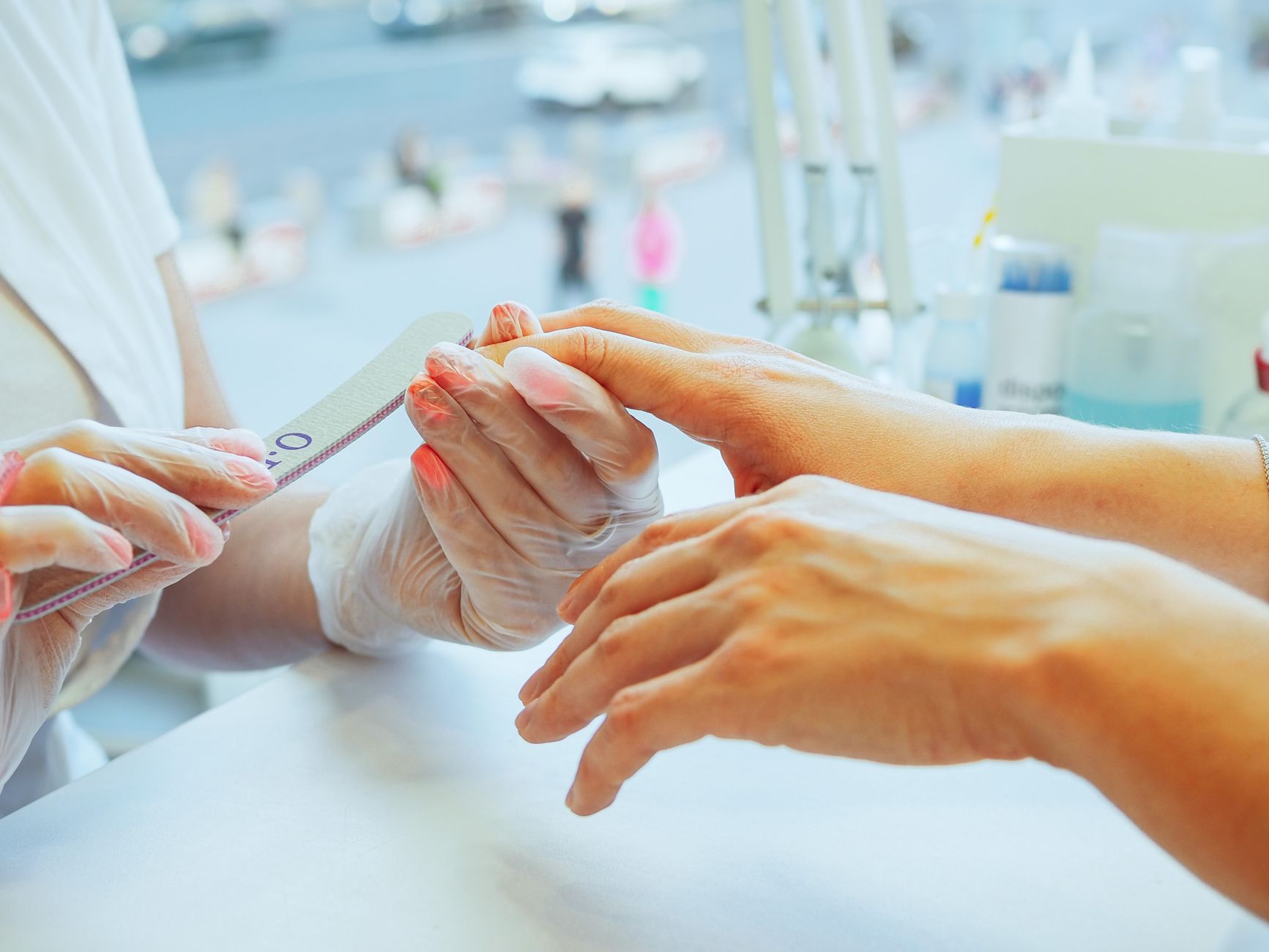 A nail technician files a client’s nails at a manicure table where fine dust and product residue can accumulate.