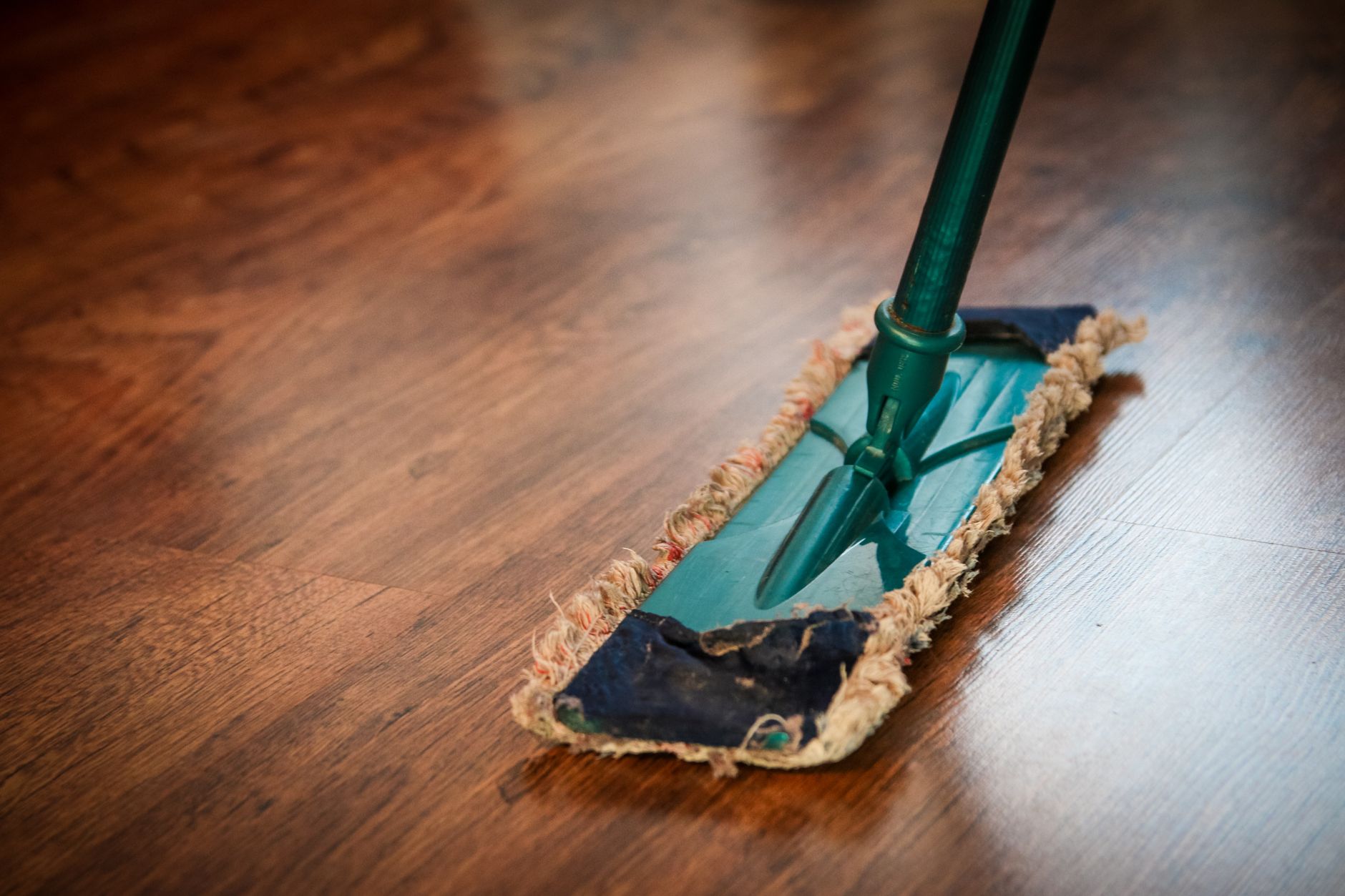 A worker uses a dry dust mop on a polished wood floor similar to a coated roller rink deck.