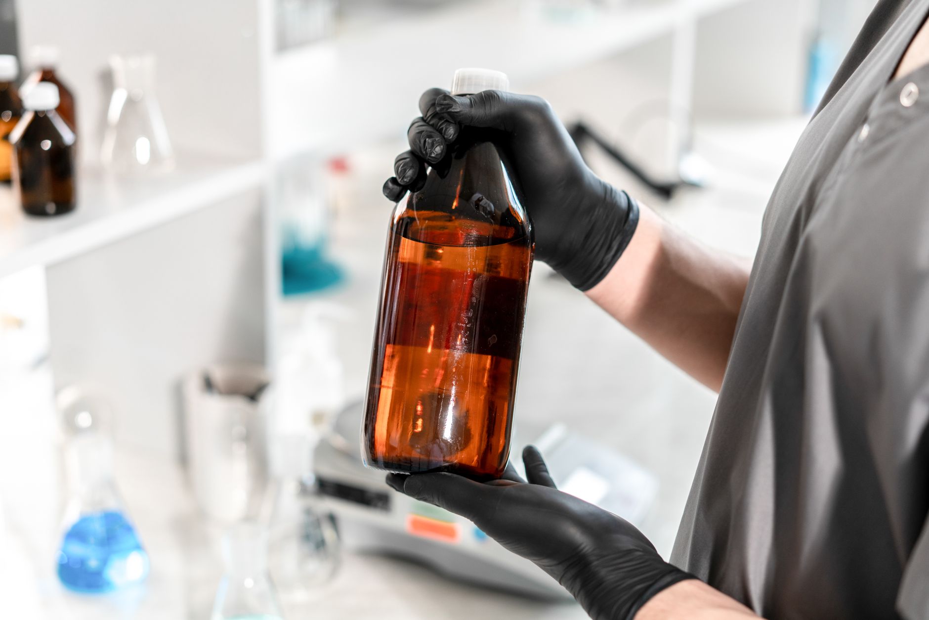 Gloved hands handle chemical containers beside protective eyewear in an industrial work area.
