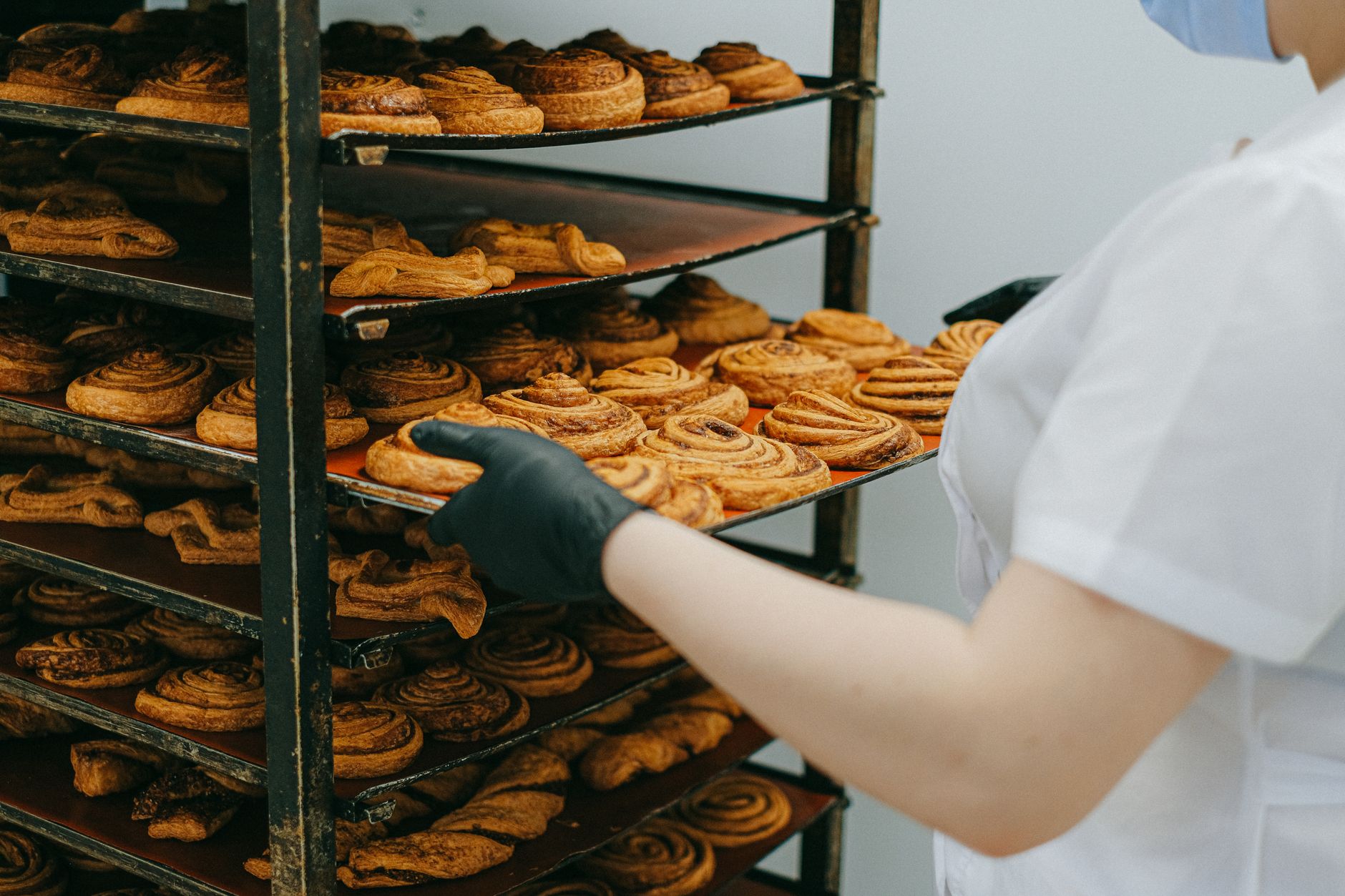 An employee loads or unloads bakery trays at a rack, illustrating a height-and-reach task that often improves with lift or tilt assistance.