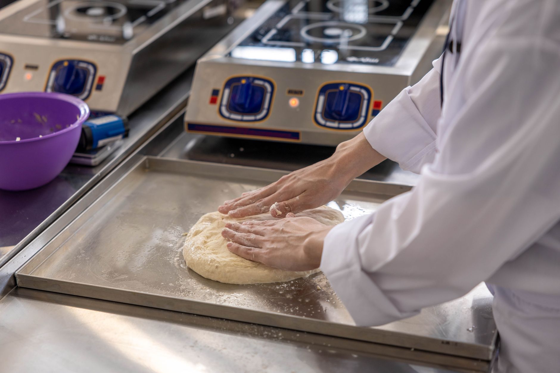 A worker cleans stainless equipment in a food-production setting, highlighting the sanitation burden that can shape packaging-line equipment choices.