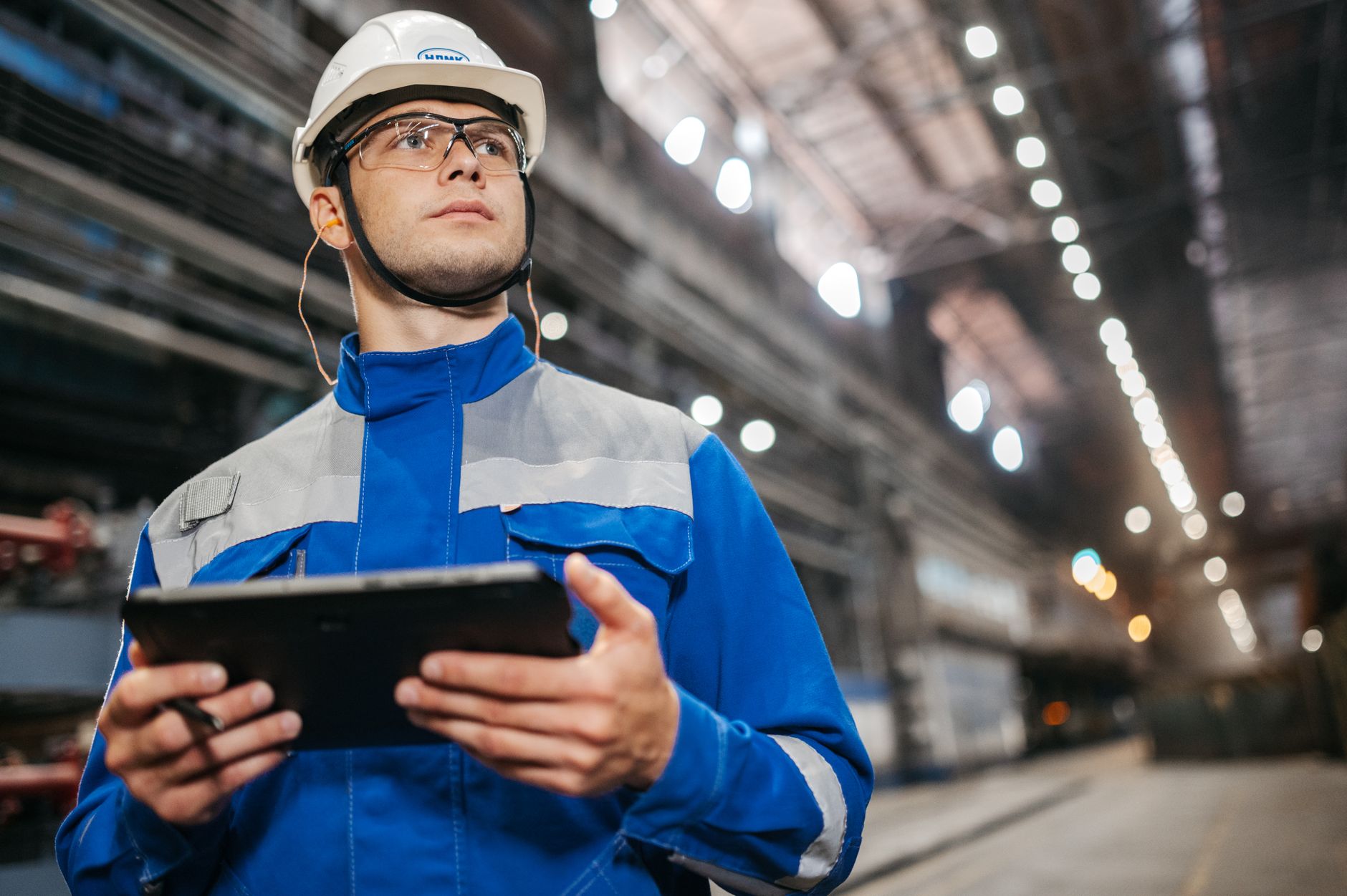 An engineer holds a tablet to interface with equipment in a factory, representing the user-friendly programming of modern cobots.