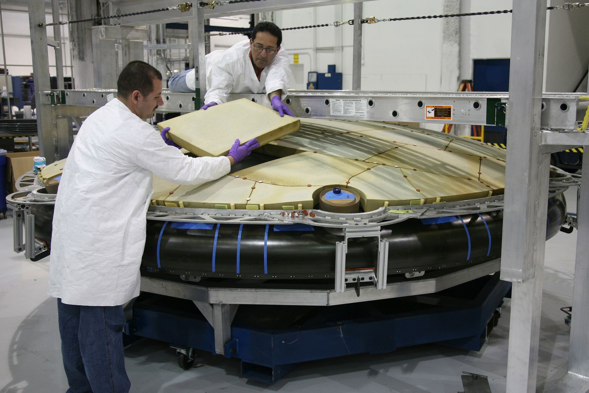 A technician carefully lays composite fabric onto a contoured mold in a manufacturing workspace.