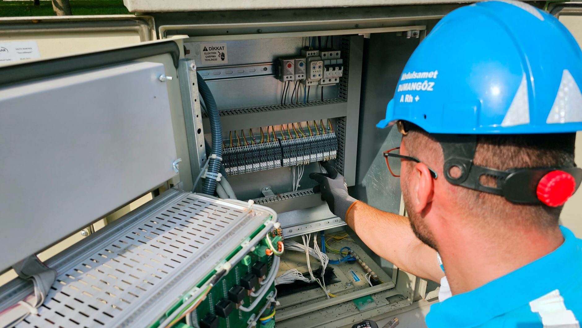An electrician wires an industrial control cabinet at a panel shop workbench.
