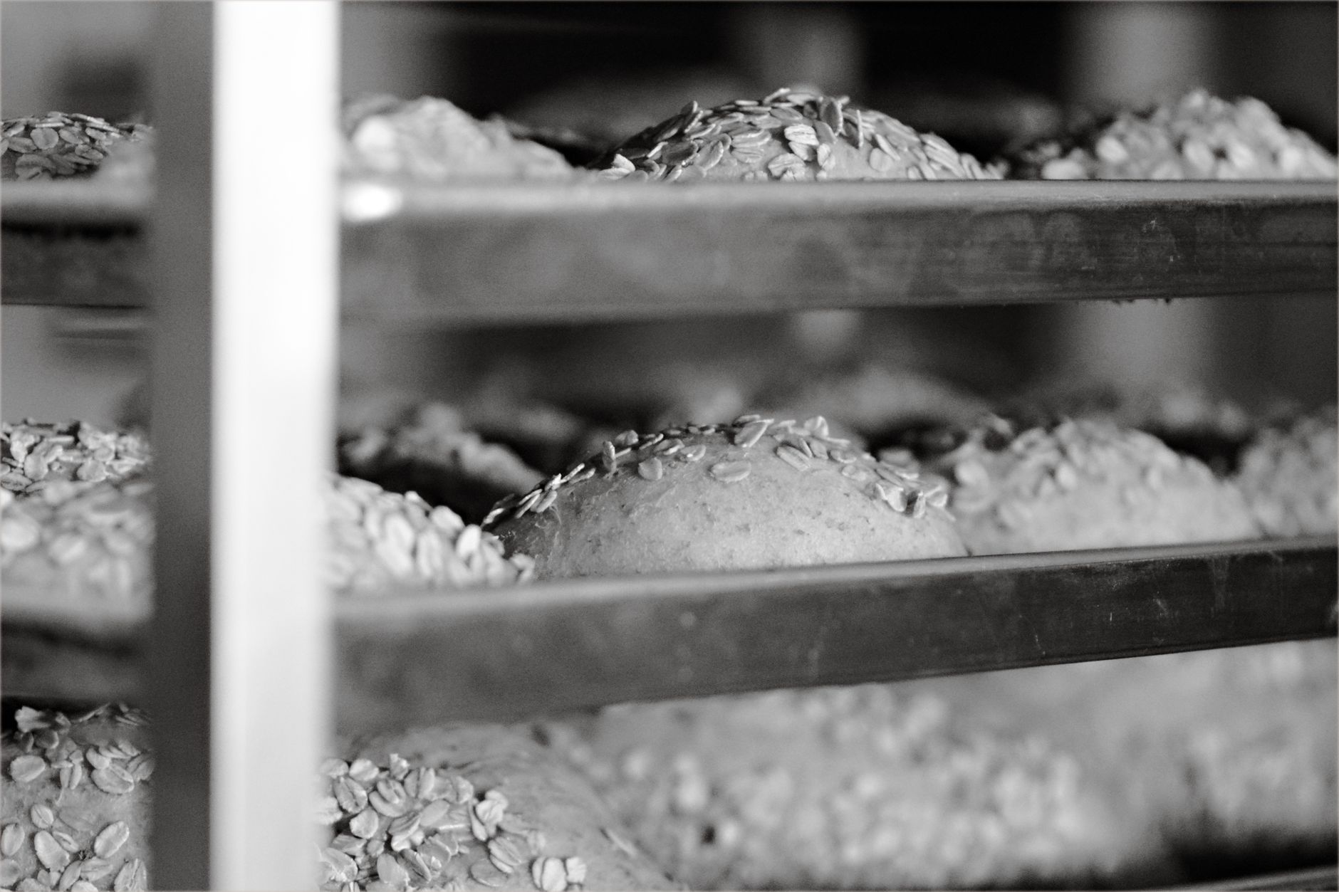 Trays of baked bread cool on tall racks while the bakery line continues operating.