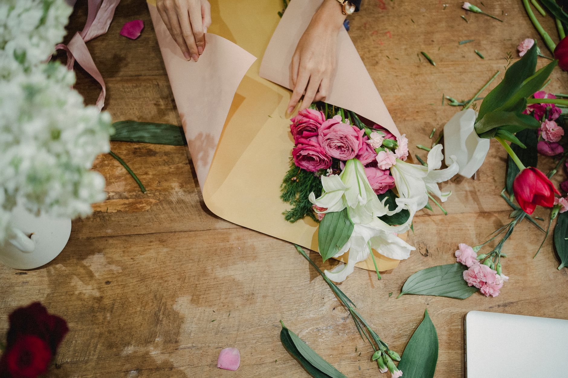 A florist wrapping stems at a counter, illustrating manual bouquet handling before automation.