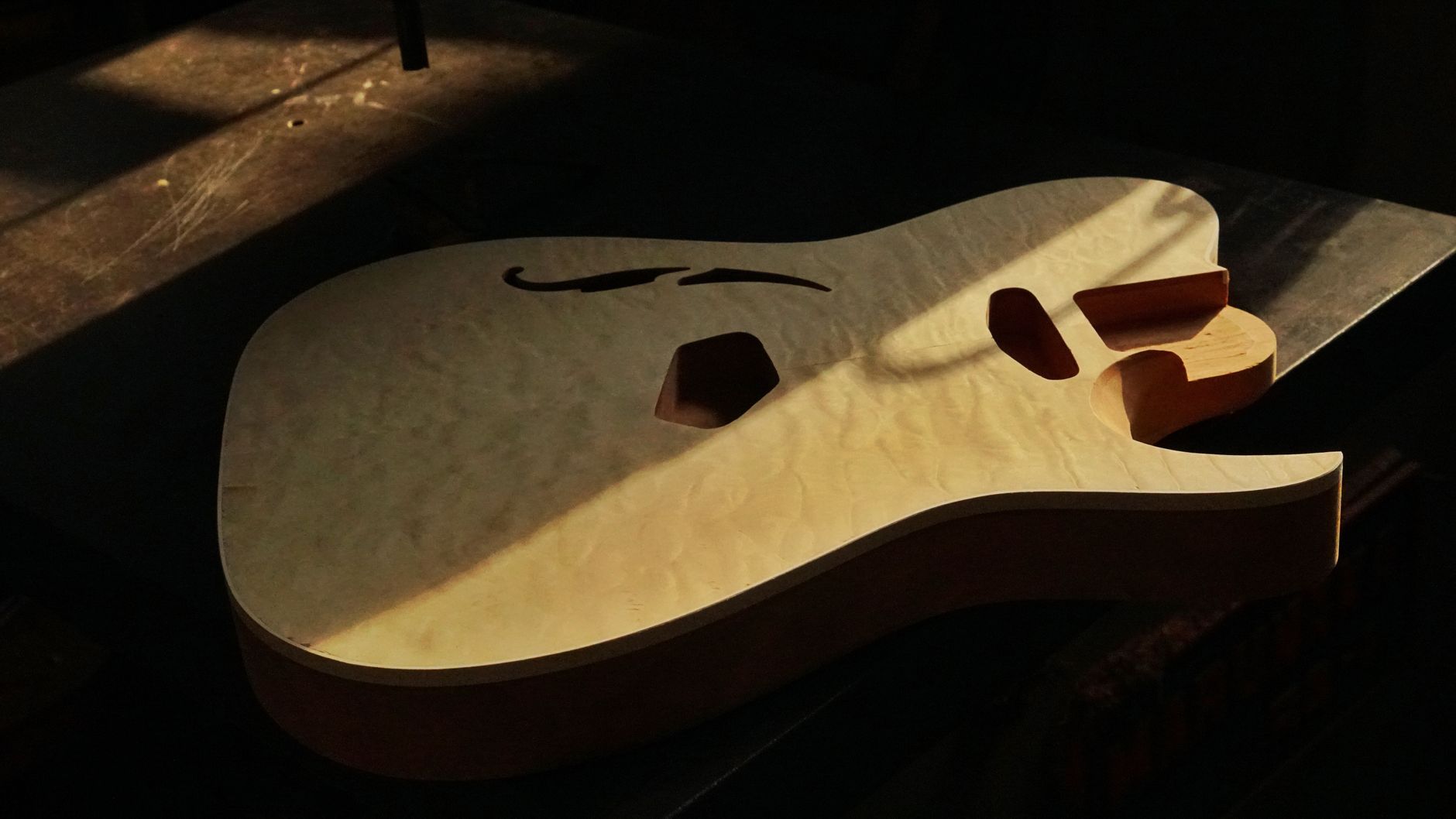 An instrument maker sands a wooden guitar body by hand, following its grain and curved edges.