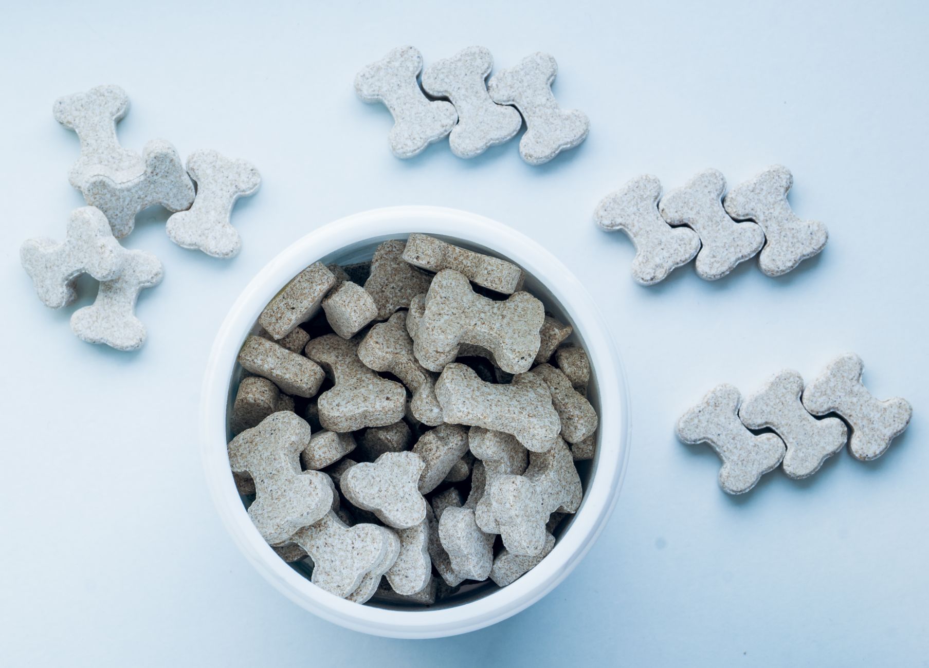 Assorted crunchy dog biscuits and chews in a bowl, showing the irregular shapes automation must grip.